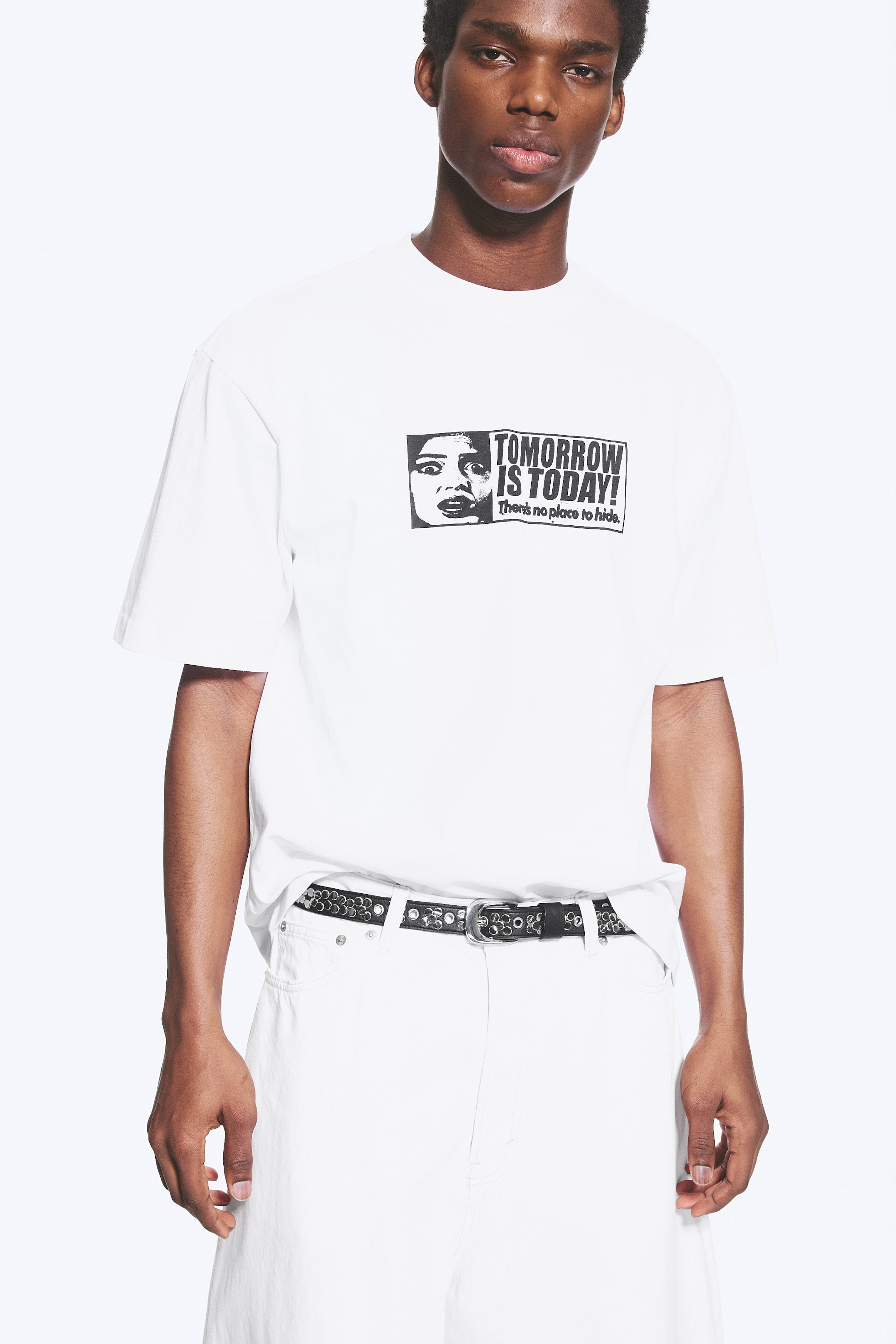 Grotere afbeelding bekijken: Een wit T-shirt toont een zwart-wit grafische print op de voorkant, waarop een gezicht met wijd opengesperde ogen en een open mond te zien is, naast de tekst 'TOMORROW IS TODAY! There's no place to hide.' Het T-shirt is ontworpen met korte mouwen en een ronde hals, en is naar voren gericht.