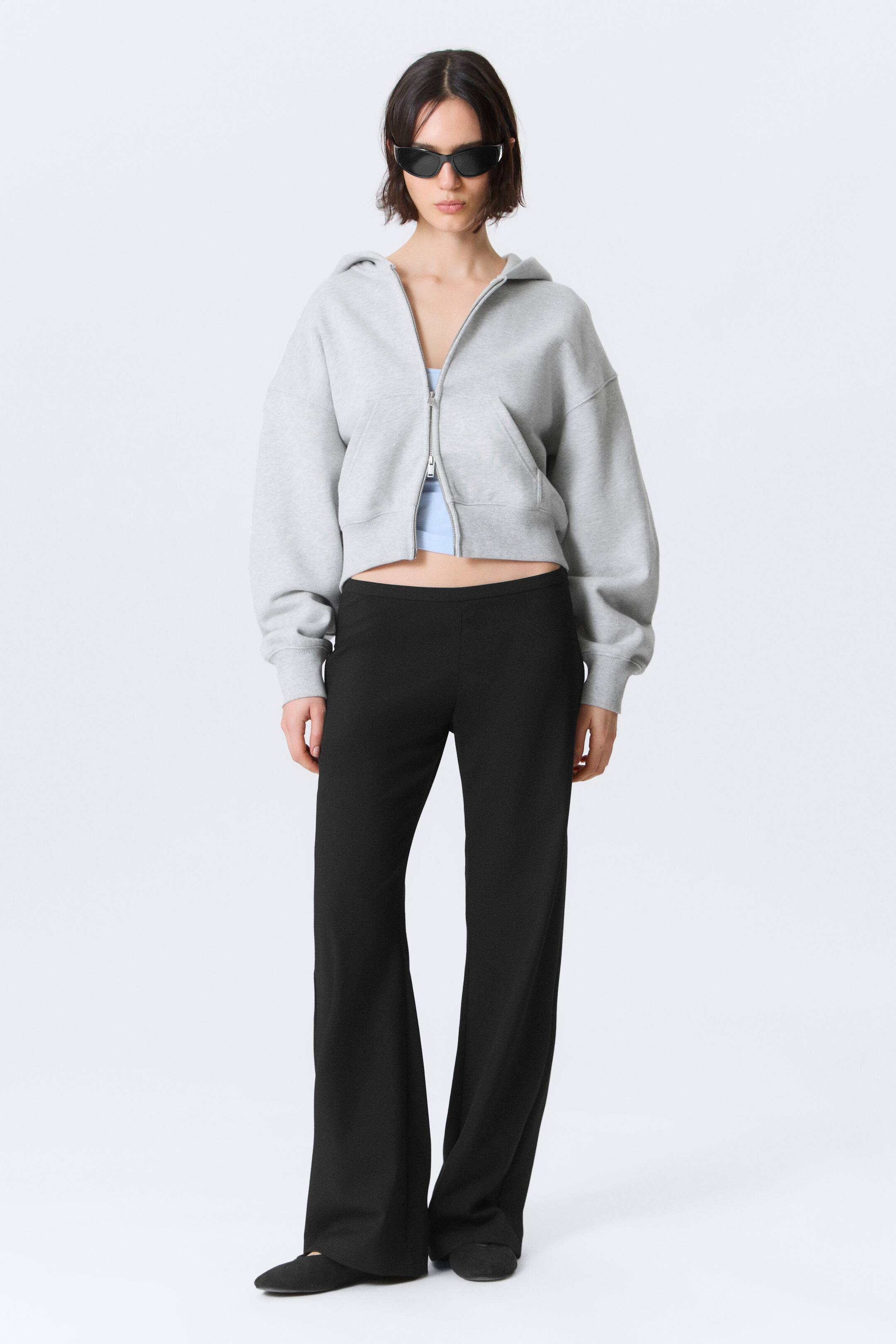Grotere afbeelding bekijken: Een grijze cropped zip-up hoodie wordt van voren gepresenteerd, met een oversized pasvorm en een rits over de volledige lengte die gedeeltelijk open is, waardoor een lichtblauw topje zichtbaar wordt. Het heeft een capuchon, geribde boorden, een geribde zoom en voorzakken in kangoeroestijl.