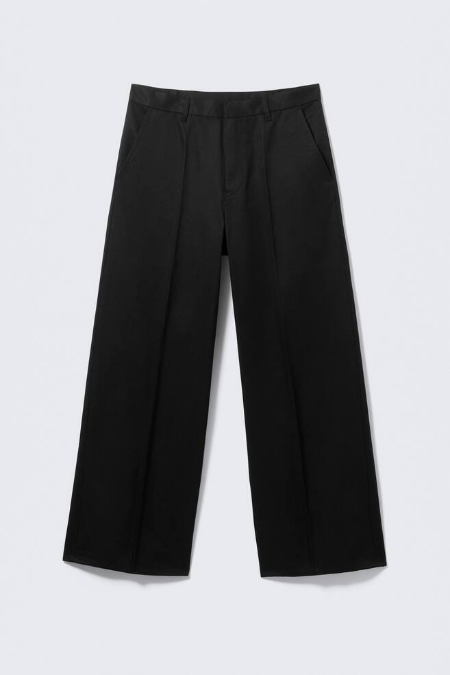Pantalon noir à jambes larges présenté de FACE, doté d'une ceinture avec passants et de poches latérales inclinées. Des plis marqués descendent le long du centre de chaque jambe large. - 1