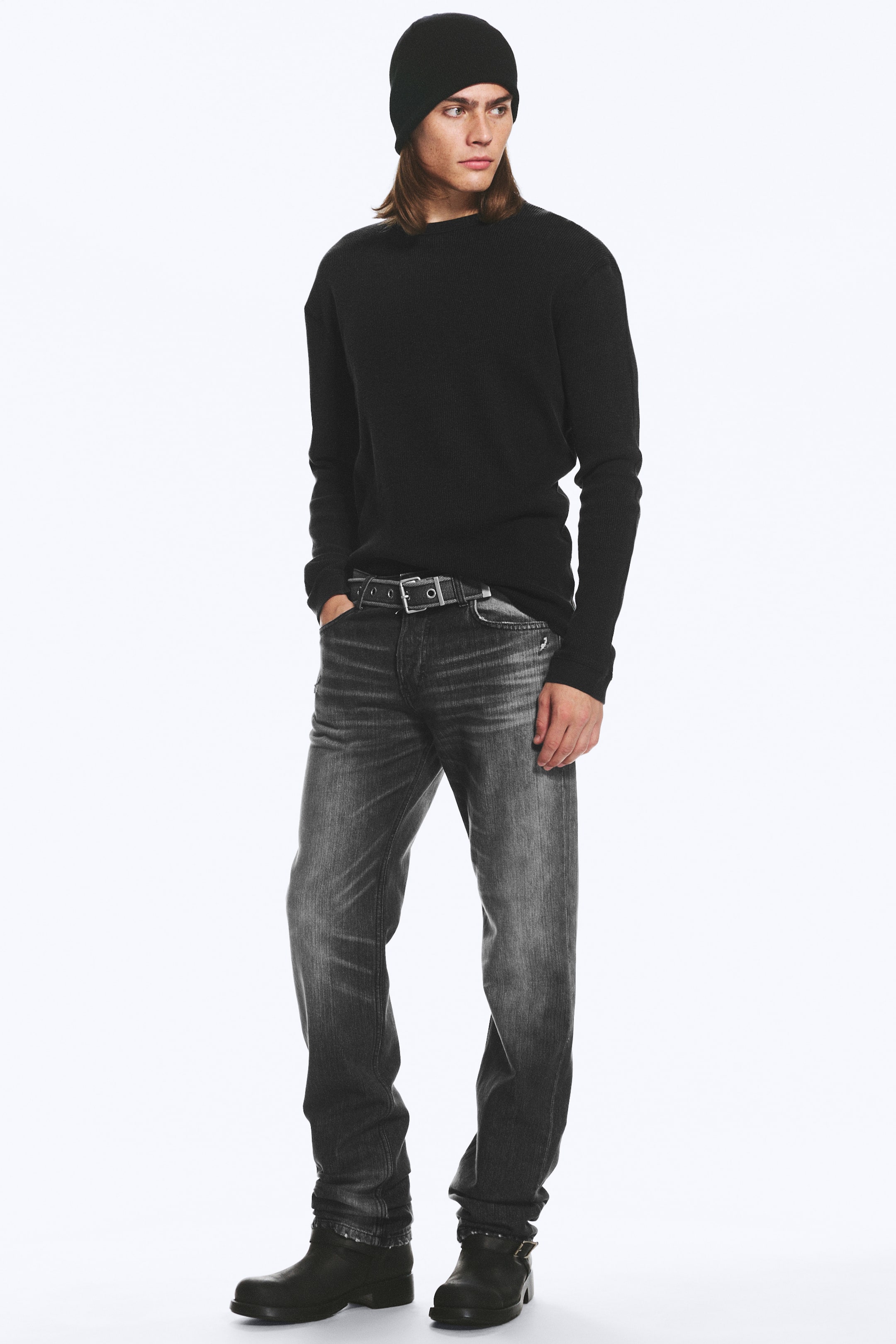 Größeres Bild anzeigen: Die Model trägt die Comet Low-Rise Slim-Fit Straight Jeans. Der dunkelgrau gewaschene Denim zeigt dezente Ausbleichungen an Oberschenkeln und Knien, und ein schwarzer Gürtel hält sie in der Taille, während eine Hand des Models in der vorderen Tasche ruht.