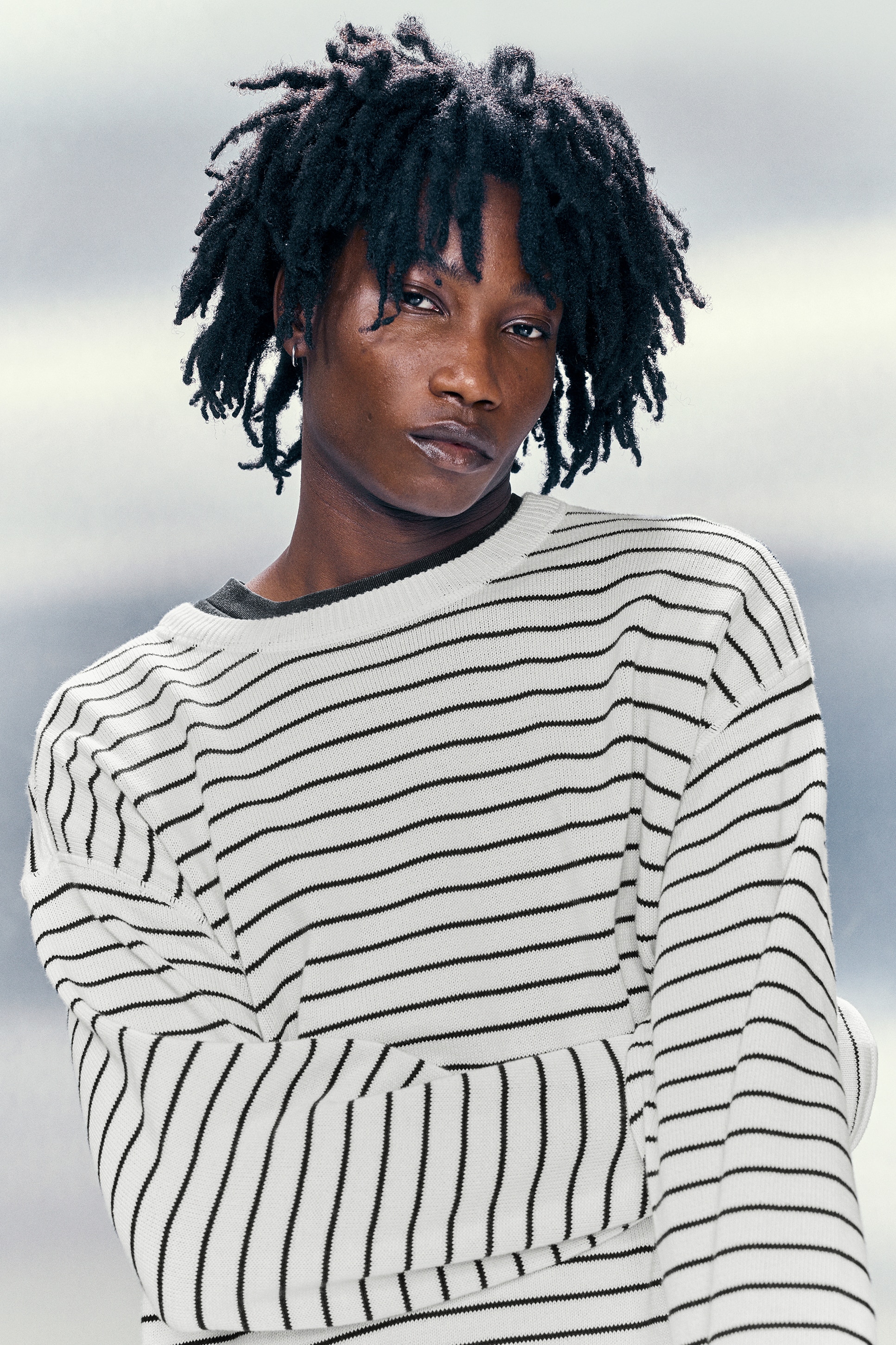 Ce pull à manches longues est rayé en blanc et noir, présenté de face. Il est doté d'un col rond côtelé, d'épaules tombantes et de poignets et ourlet côtelés.