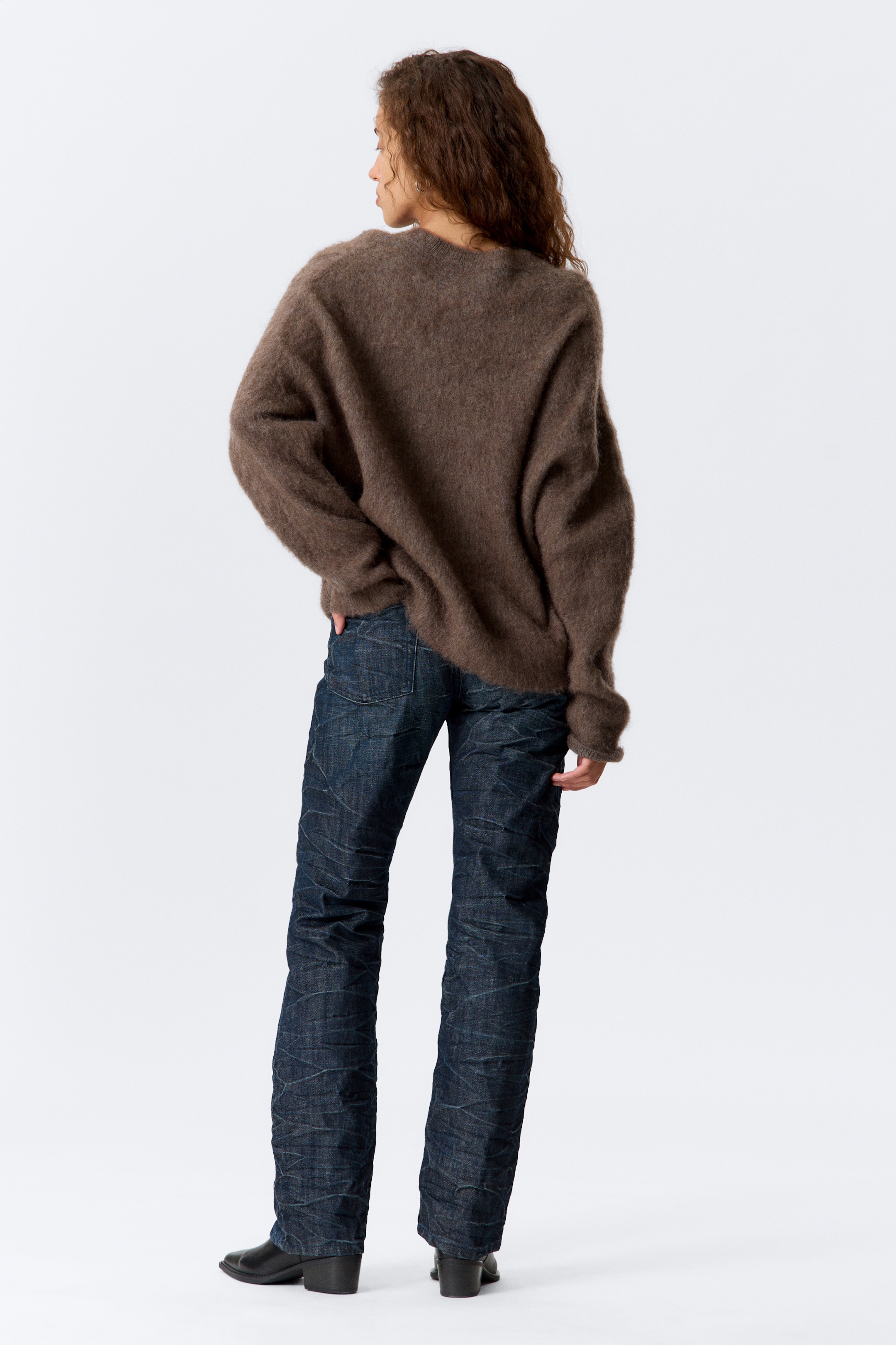 Größeres Bild ansehen: Ein brauner, flauschiger, übergroßer Pullover wird getragen, der eine lockere Passform und lange Ärmel aufweist. Er wird mit dunkel indigo Jeans kombiniert, die eine geknitterte Textur und einen geraden Schnitt präsentieren, von hinten betrachtet.