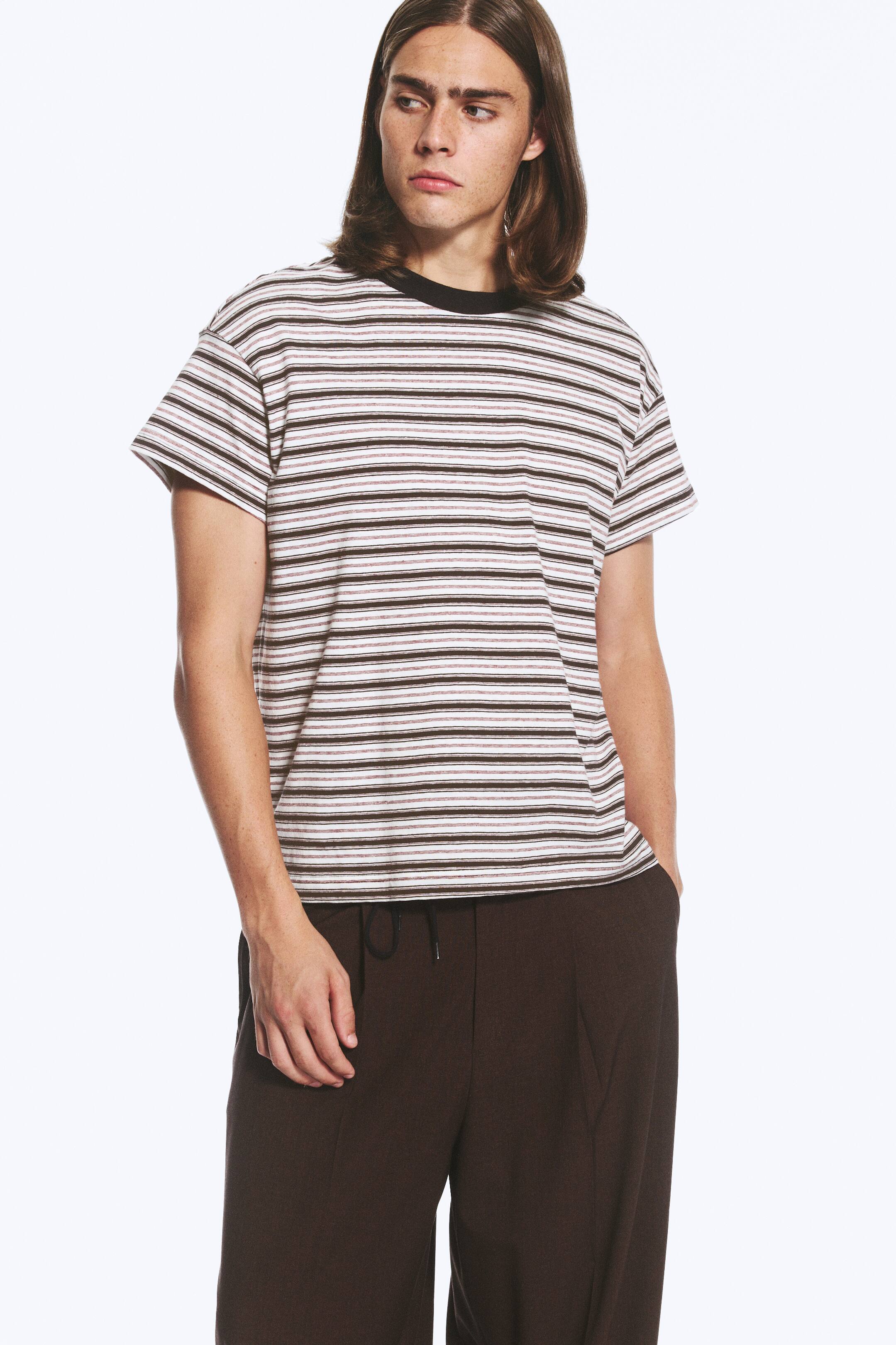 Größeres Bild ansehen: Das Model trägt ein kastig geschnittenes T-Shirt mit verblassten Streifen in Weiß, Dunkelbraun und Rotbraun. Es verfügt über einen ausgewaschenen schwarzen Rippkragen, überschnittene Schultern und kurze Ärmel, wodurch eine lässige Silhouette entsteht.