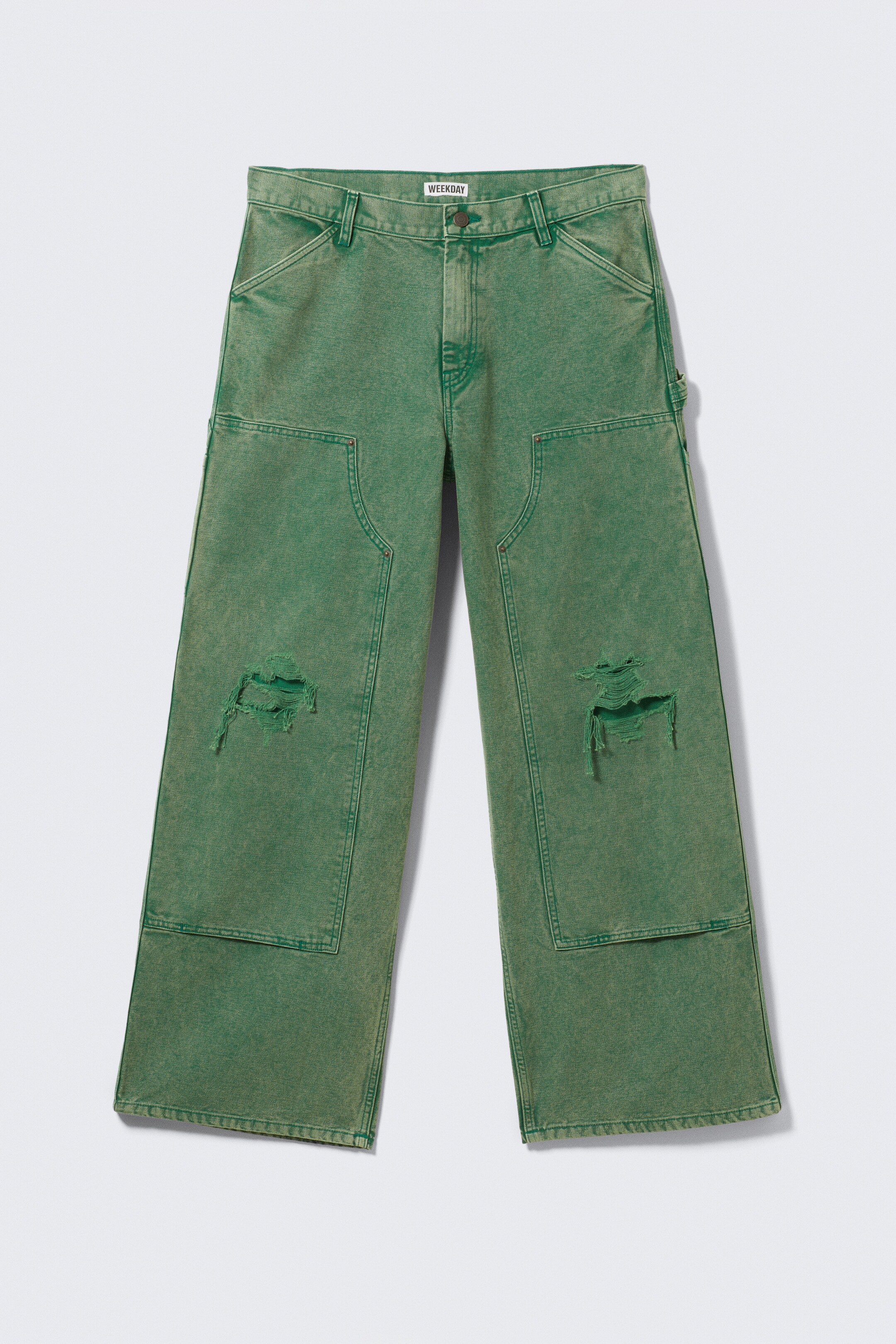 Vezi imaginea mai mare: O pereche de pantaloni utilitari supradimensionați, de culoare verde spălat, este prezentată din FAȚĂ, având o talie joasă și picioare largi. Aceștia prezintă buzunare mari aplicate, genunchi cu aspect uzat, un inel pentru ciocan pe lateral și cusături vizibil întărite care indică o construcție durabilă.