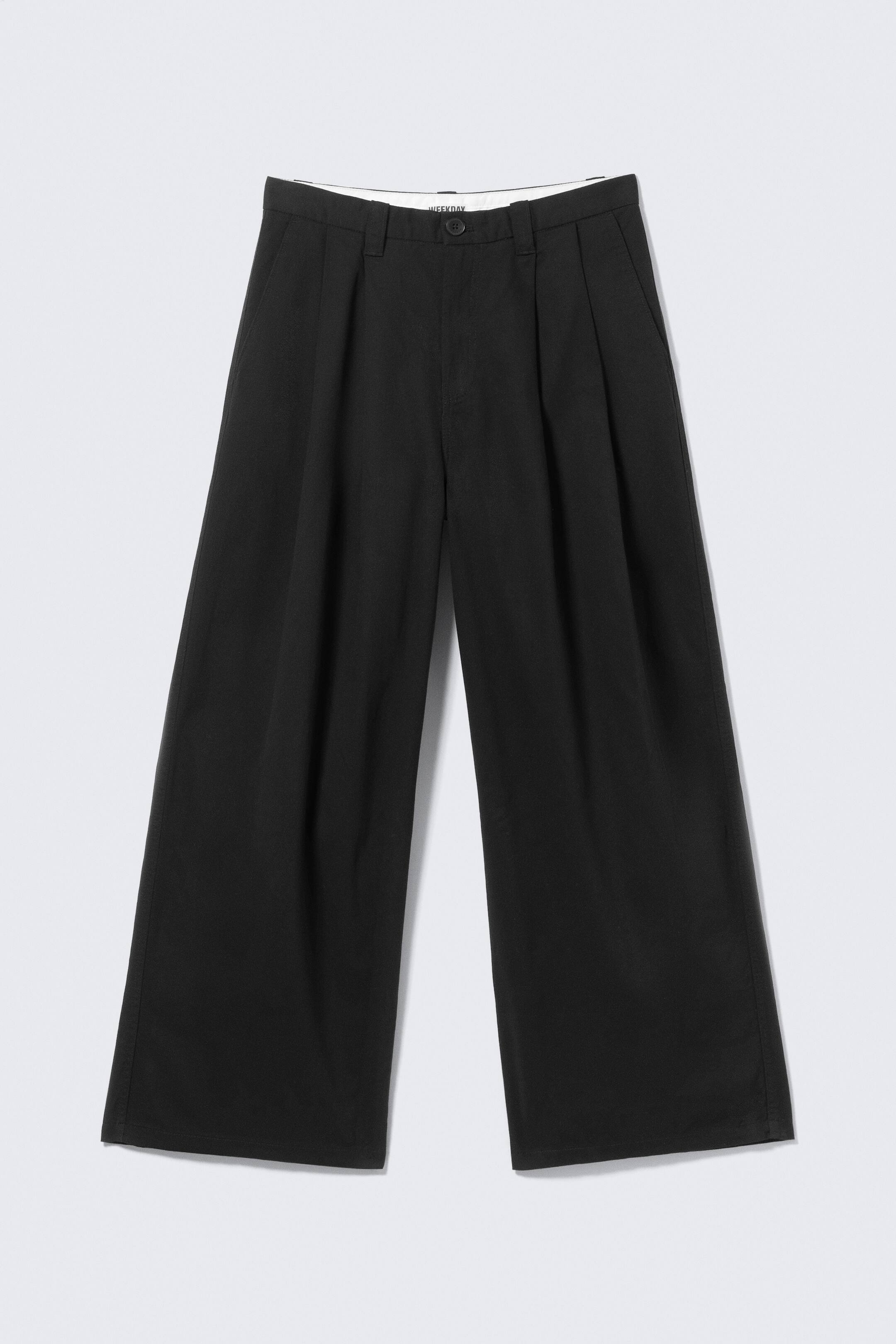 Agrandir l'image: Le pantalon noir est présenté de face, avec une ceinture structurée dotée de passants pour ceinture et d'une fermeture à bouton. Il met en avant des plis simples et marqués de chaque côté, se prolongeant dans un design à jambes larges.