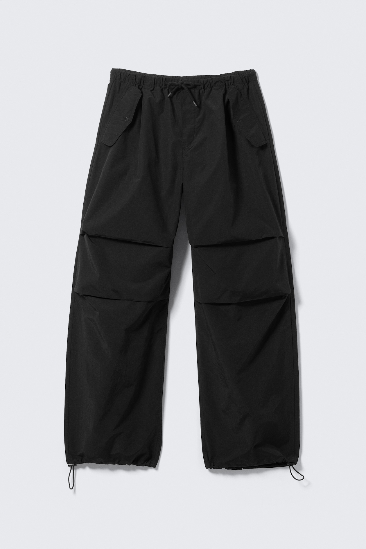 Black parachute pants laid flat with clearly visible horizontal knee pleats