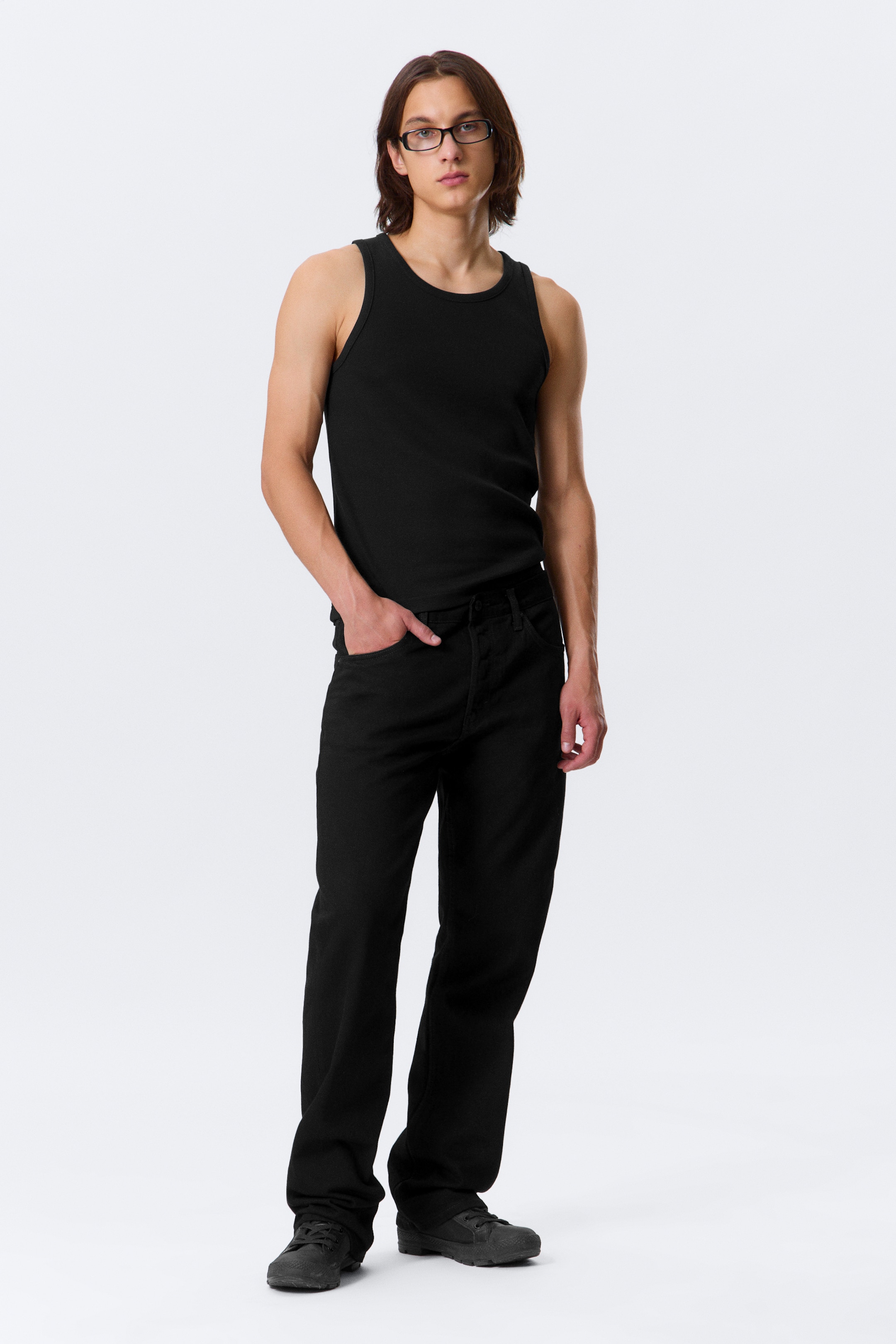View larger image: A black ribbed tank top is being worn, featuring a crew neck and sleeveless design, visible from a slight front angle. It is paired with black straight-leg pants, which include visible front pockets, and black lace-up low-top shoes.