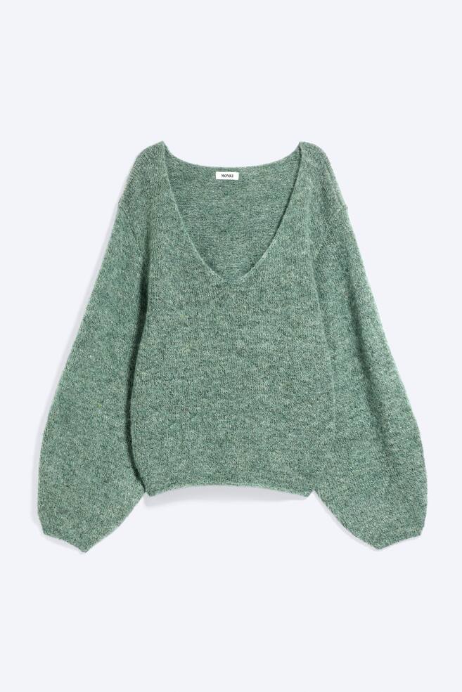 Un pulover tricotat oversized Ã®ntr-o nuanÈÄ de verde melanj este prezentat din faÈÄ, avÃ¢nd un decolteu adÃ¢nc Ã®n V Èi umeri cÄzuÈi. Designul relaxat evidenÈiazÄ mÃ¢neci voluminoase, o siluetÄ lejerÄ Èi margini ribate la manÈete Èi la tiv. - 1