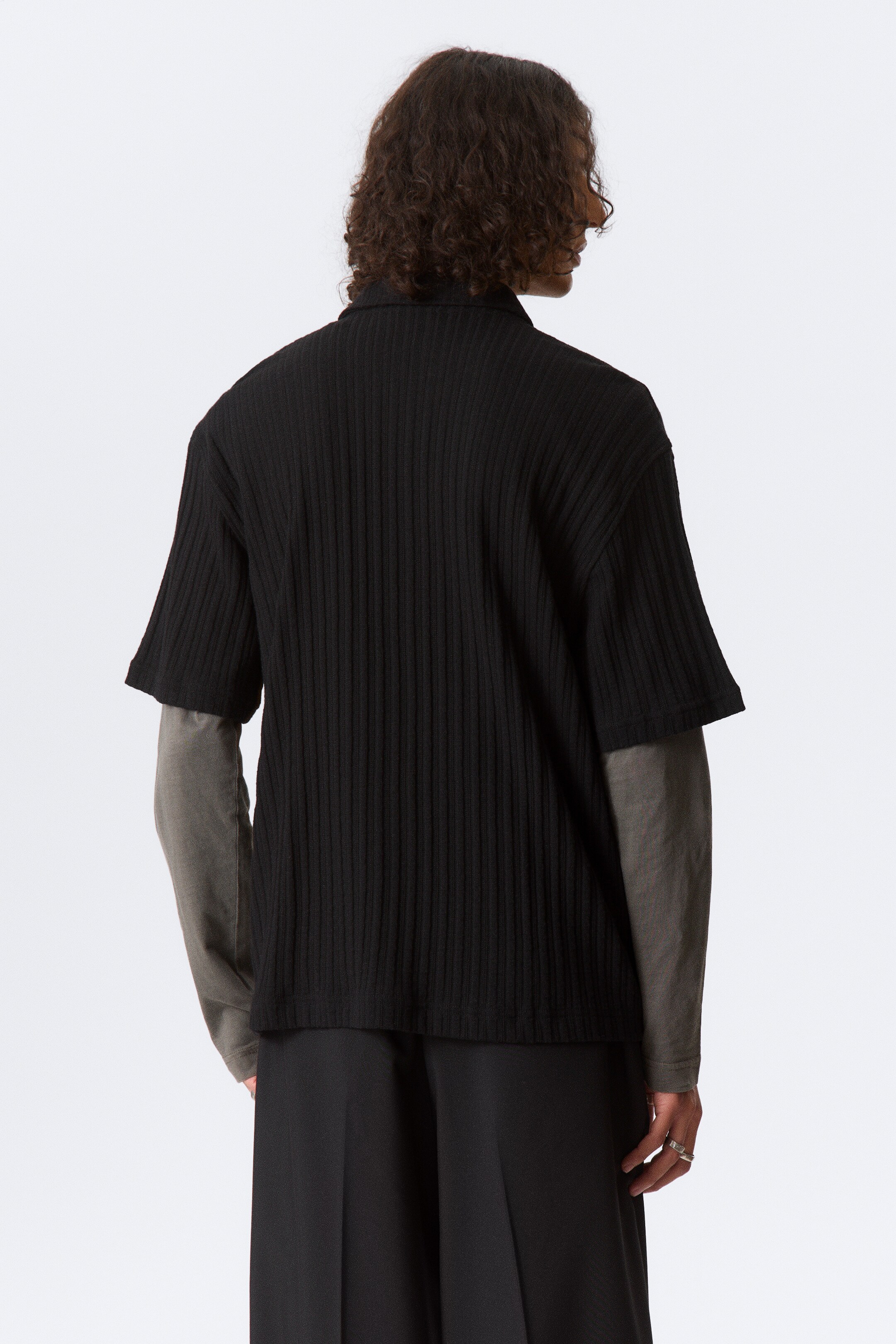 Vezi imaginea mai mare: Un tricou negru cu mâneci scurte și cu nervuri își prezintă partea din spate, fiind suprapus peste un tricou gri cu mâneci lungi. Tricoul are un guler polo și nervuri verticale distincte pe tot materialul său.