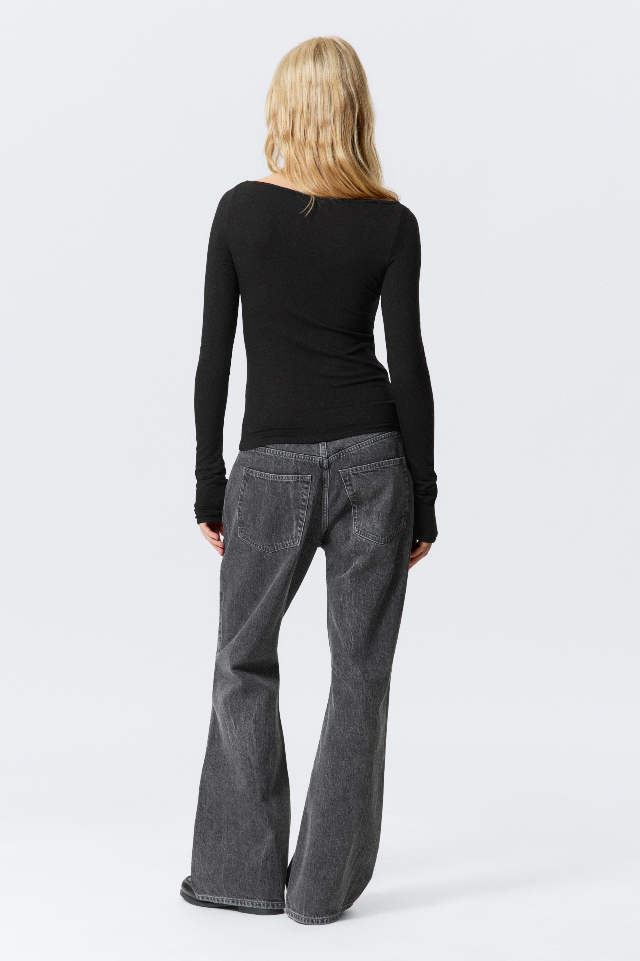 Größeres Bild anzeigen: Ein schwarzes langärmliges Oberteil und dunkelgraue Jeans mit weitem Bein werden von hinten gezeigt. Das schwarze Oberteil zeichnet sich durch eine schmale Passform, eine gerippte Textur, einen breiten U-Boot-Ausschnitt und extra lange Ärmel aus, die über die Hände reichen. Die dunkelgrauen Jeans präsentieren ein gewaschenes Denim-Aussehen und einen weiten Schnitt, der sich an den Knöcheln sammelt.
