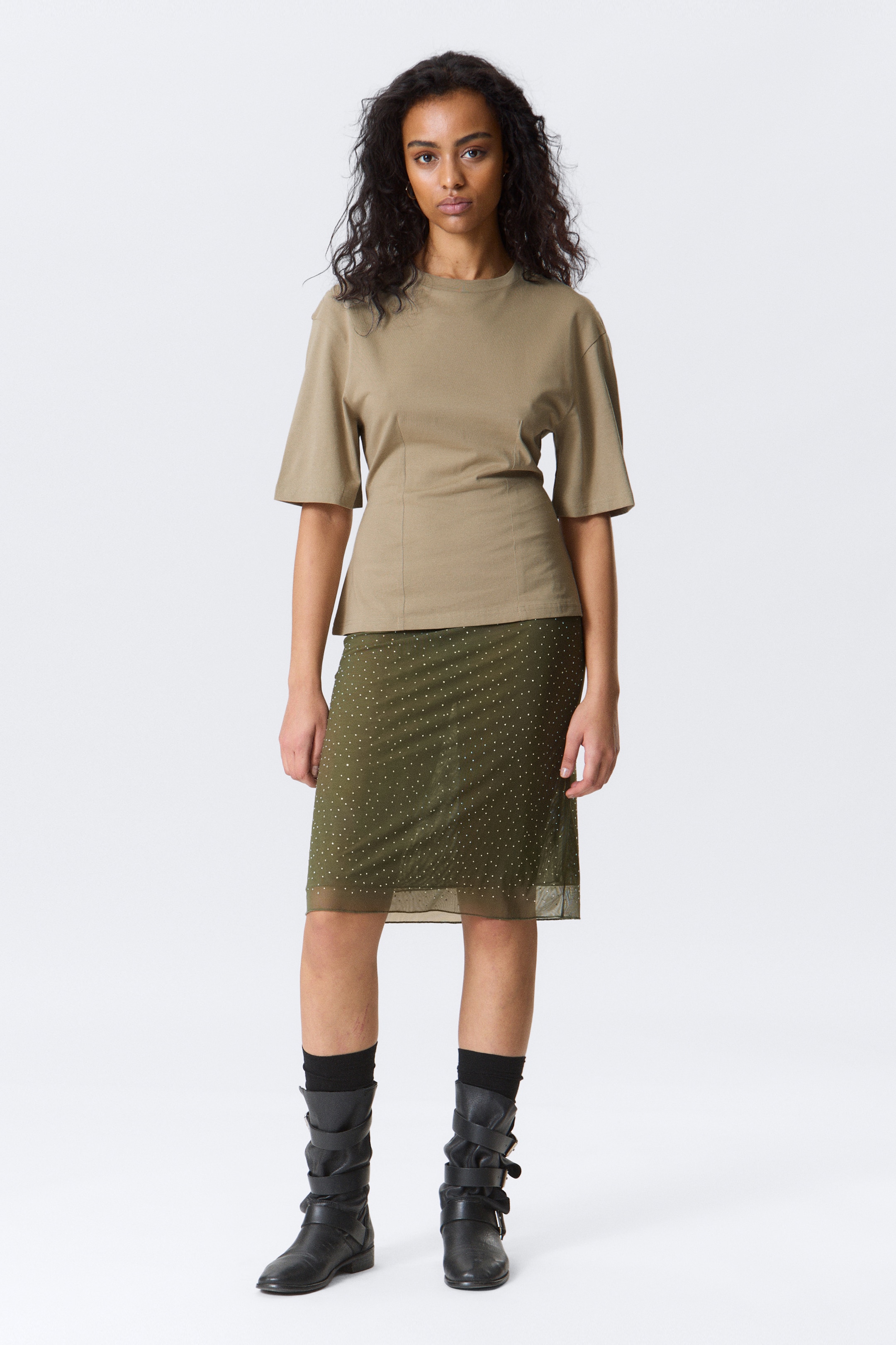 Zobrazit větší obrázek: Modelka má na sobě khaki přiléhavé tričko s rukávy po lokty. Kulatý výstřih rámuje krk a spadlá ramena tvarují horní část. Jemné detaily švů vytvářejí siluetu, která obepíná tělo.