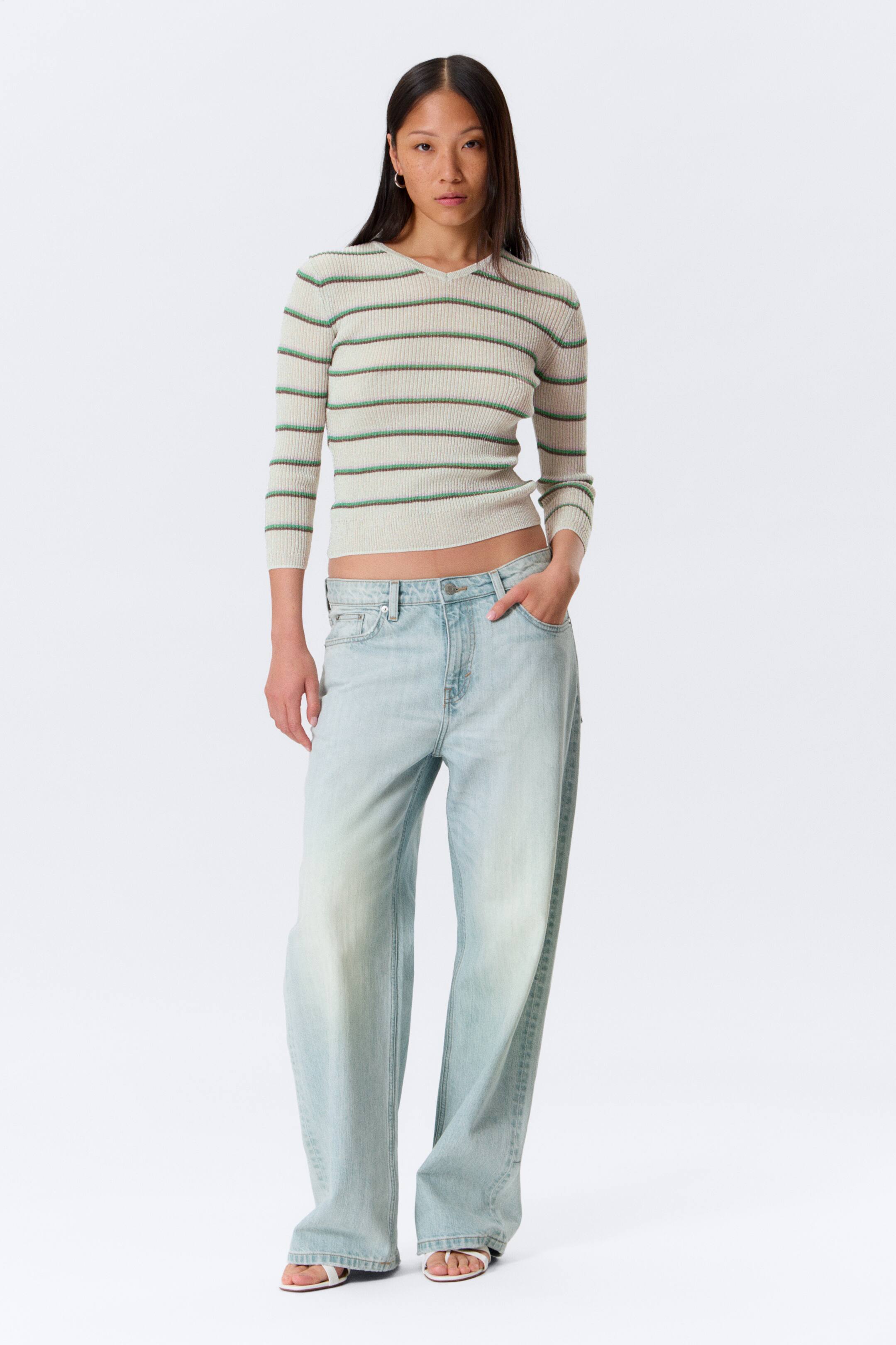 Vis større bilde: En beige ribbestrikket topp med horisontale grønne striper, V-hals og trekvart ermer, som gir en kort, tettsittende silhuett. Til dette komplementerer lysvaskede, løstsittende jeans med vide ben, som har lav midje og full lengde.