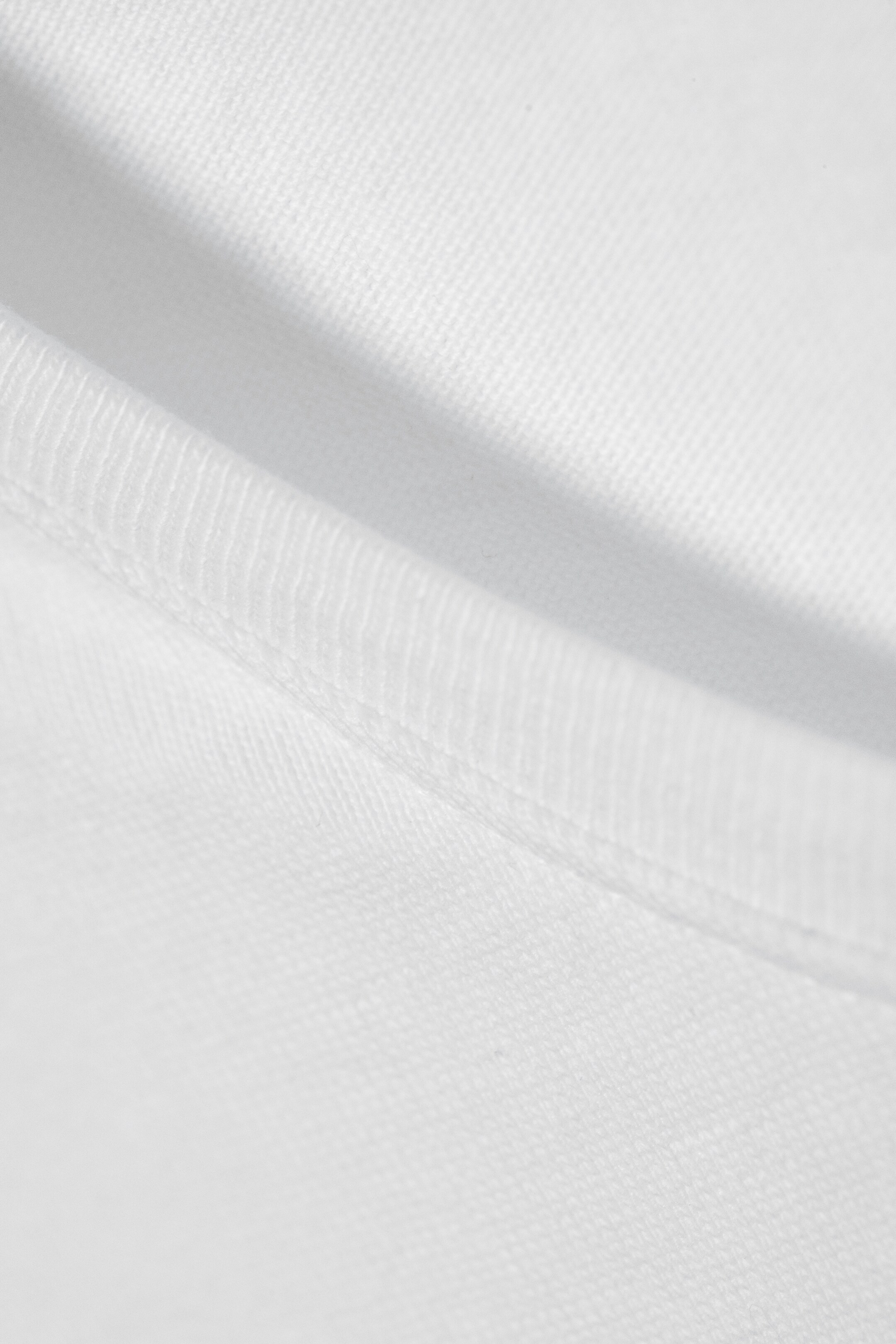 View larger image: A white fabric detail is showing a ribbed section connecting via a seam to a finely textured fabric, with the stitching clearly visible.