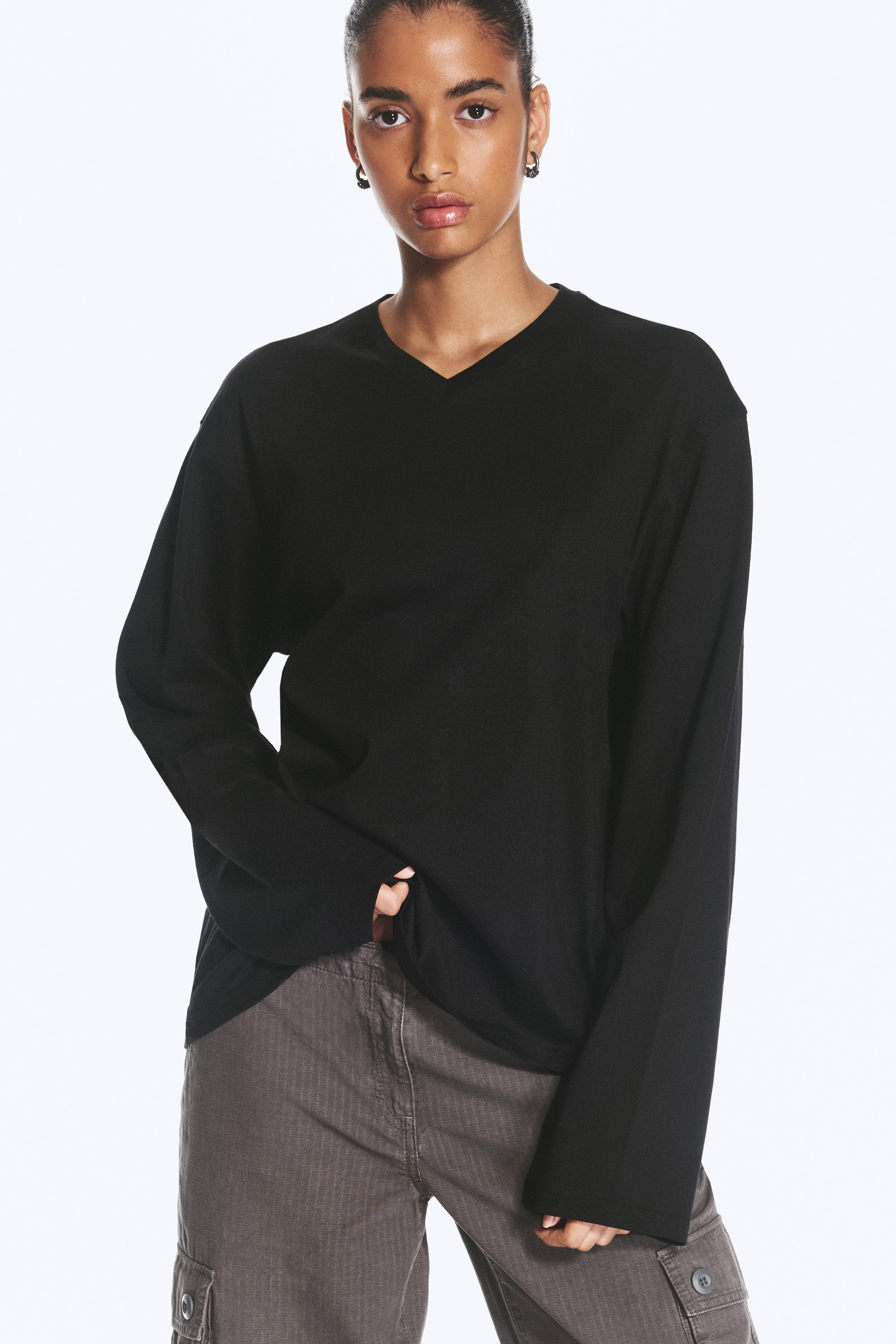 Una camiseta negra de manga larga, de corte boxy y cuello en V, vista de frente, que muestra una silueta relajada con hombros caÃ­dos y mangas anchas y holgadas. La prenda presenta un clÃ¡sico escote en V y un bajo recto y limpio.