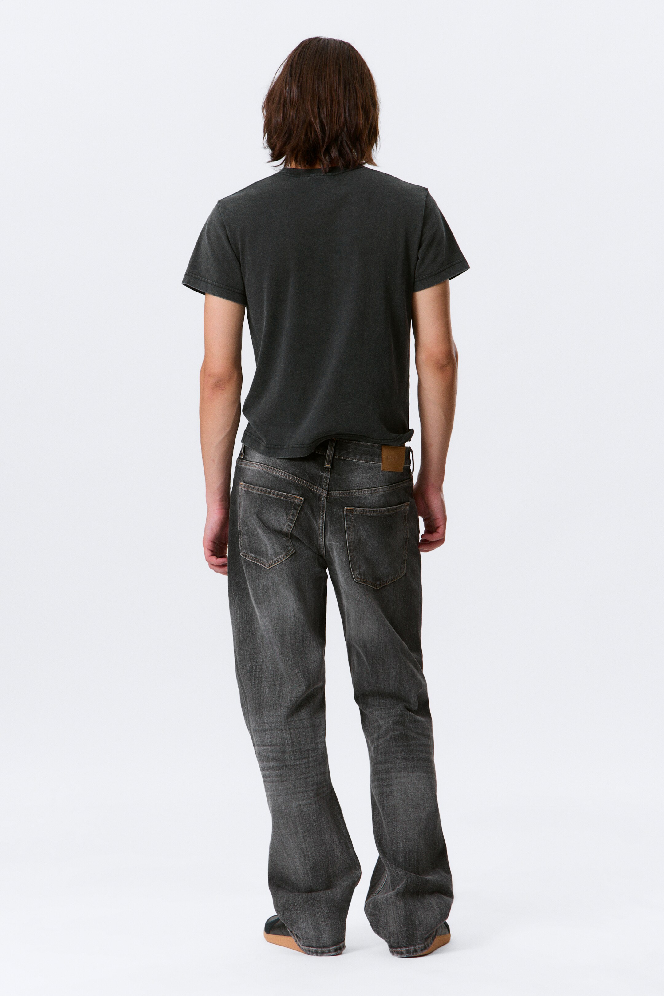 Größeres Bild ansehen: Ein dunkelgraues, gewaschenes T-Shirt und dunkelgraue Jeans mit entspannter Passform werden von hinten präsentiert. Das kurzärmelige T-Shirt zeigt einen Rundhalsausschnitt und einen ungesäumten Saum, während die Jeans sichtbare Gesäßtaschen, einen braunen lederähnlichen Aufnäher am rechten hinteren Bund aufweisen und mit einem weiten, geraden Bein fallen.