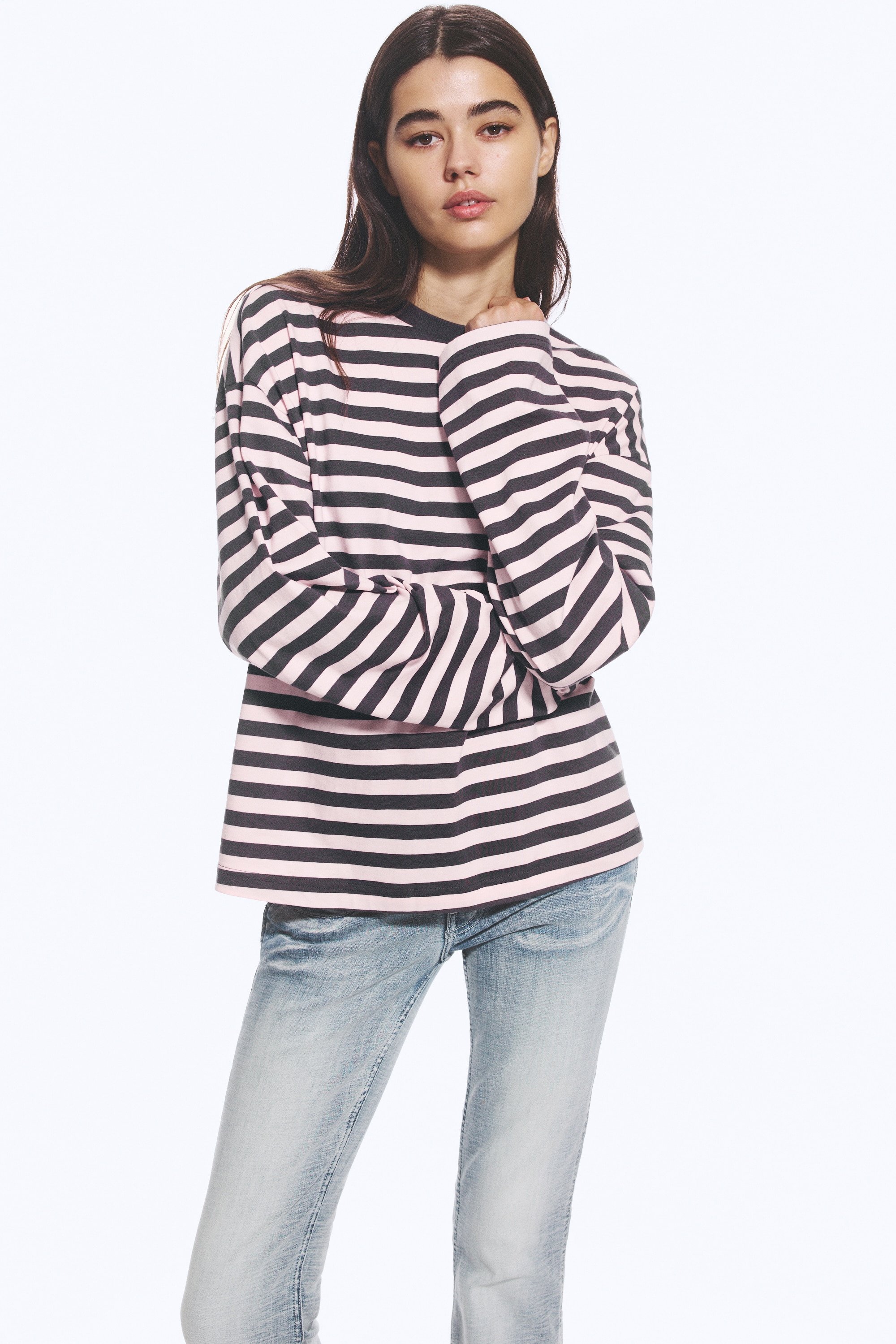 Una T-shirt a maniche lunghe a righe Ã¨ mostrata frontalmente, con strisce orizzontali alternate rosa e grigio scuro. Presenta una silhouette rilassata con spalle scese, maniche ampie e un girocollo a costine in contrasto di colore grigio scuro.