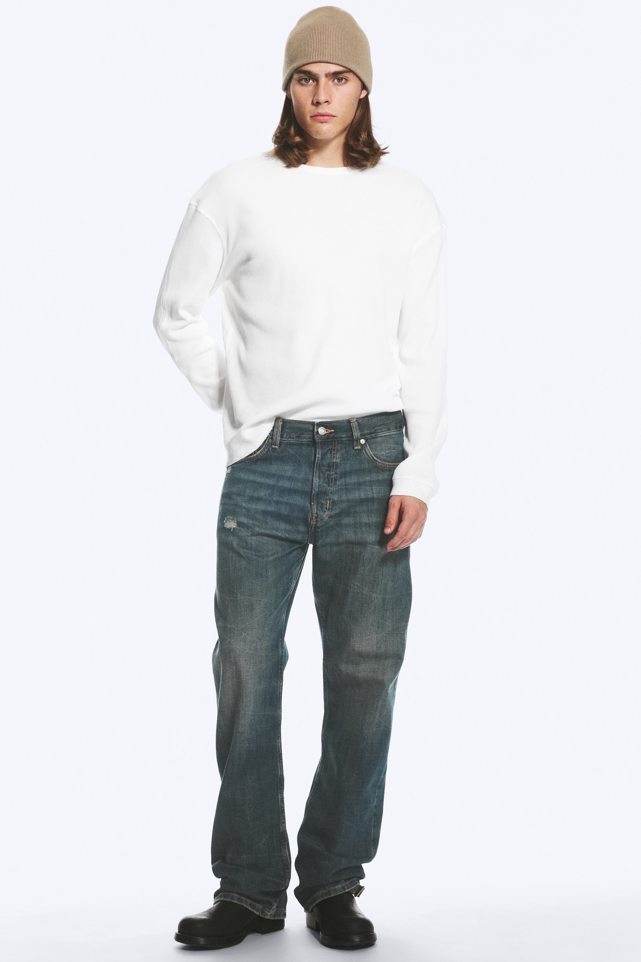 Visualizza l'immagine ingrandita: Jeans a vita media in lavaggio blu sbiadito, con vestibilità rilassata e gamba dritta, indossati dalla modella. I jeans presentano il classico design a cinque tasche e sono abbinati a una camicia bianca a maniche lunghe infilata nella cintura e stivali neri.