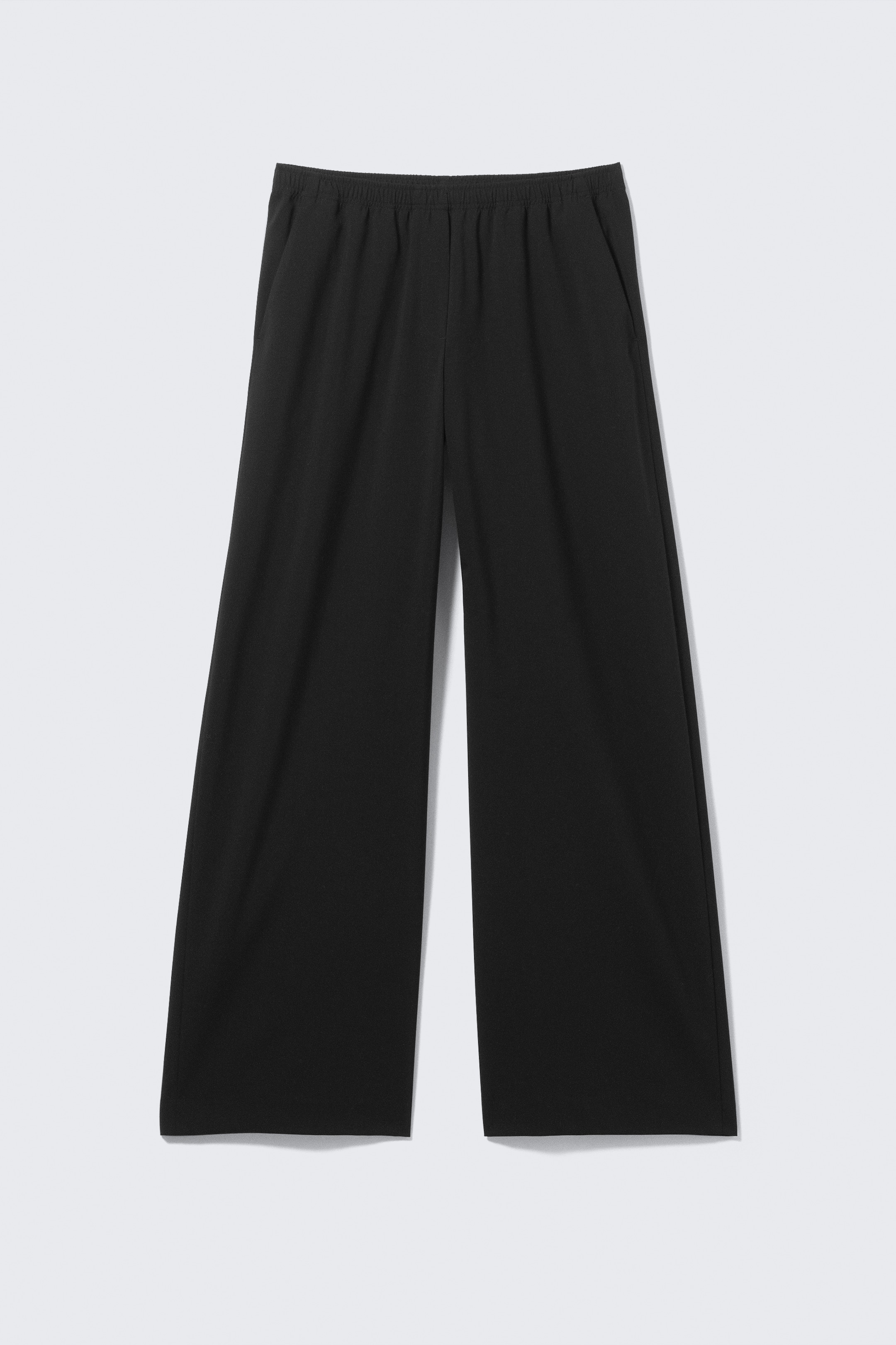 Grösseres Bild ansehen: Eine schwarze weite Hose wird von vorne gezeigt, mit einem elastischen Bund und schrägen Seitentaschen.