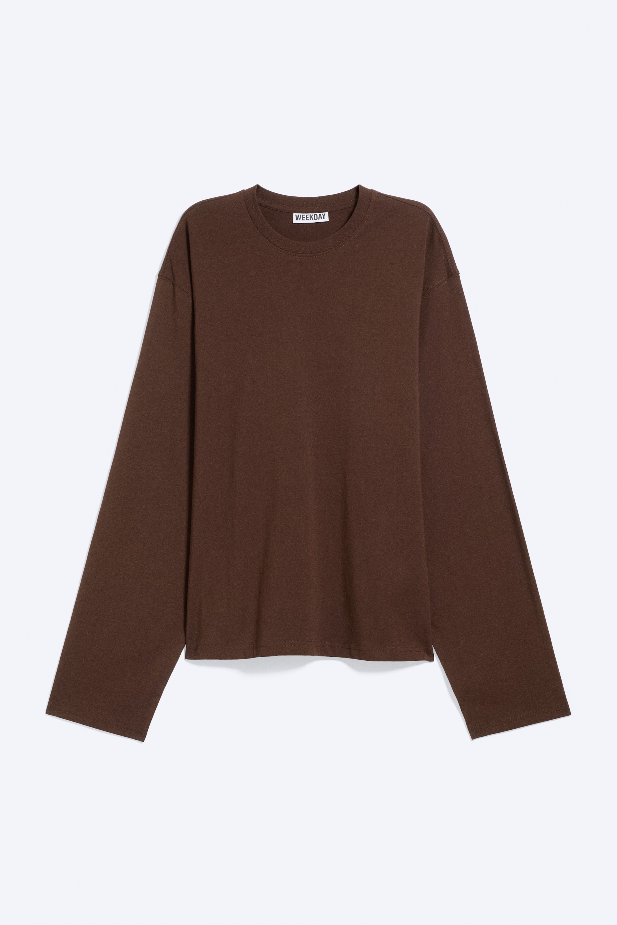 Visa större bild: En brun långärmad T-shirt visas framifrån, tillverkad i mjuk bomullsjersey och skuren i en lös, boxig passform. Den har en rund ribbad halsringning och en rak fåll.