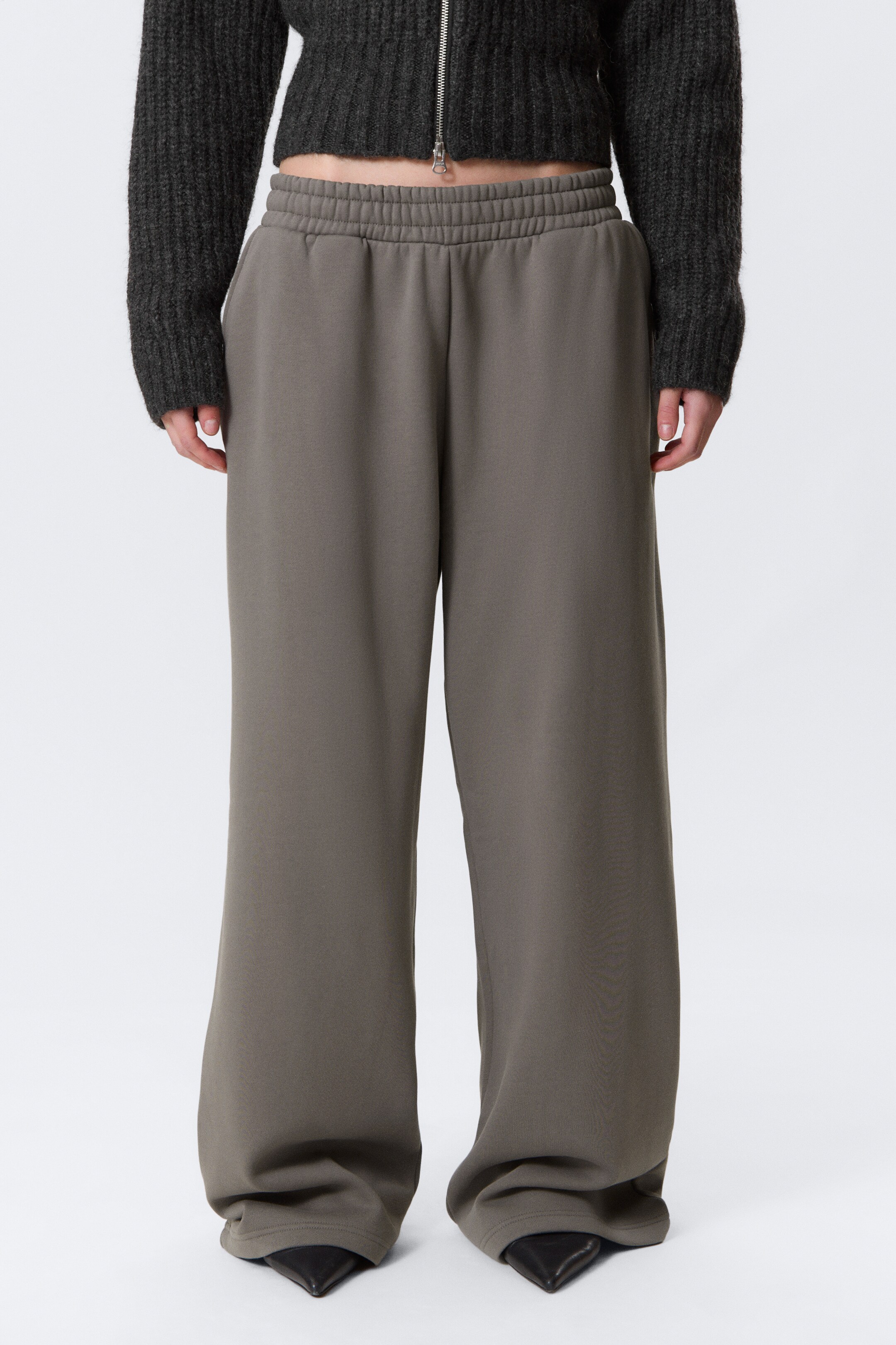 Ver imagen más grande: Un par de pantalones de pierna ancha y ajuste relajado en un color gris-verde apagado se muestra desde una vista frontal. Los pantalones presentan una cintura elástica fruncida, bolsillos laterales sutiles y se extienden a lo largo completo, cayendo ligeramente sobre los zapatos del usuario.