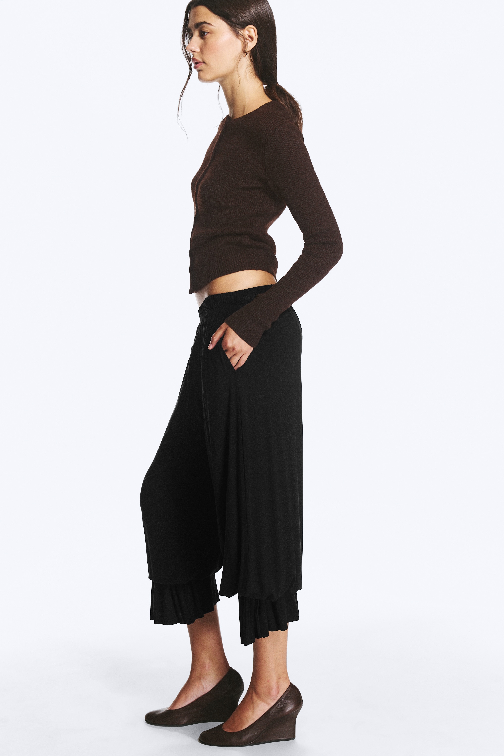 "Pantaloni a palloncino in jersey nero con cintura elasticizzata e gambe ampie, visti frontalmente. Gli orli delle gambe si raccolgono alle caviglie, con dettagli regolabili a laccio sui lati esterni."