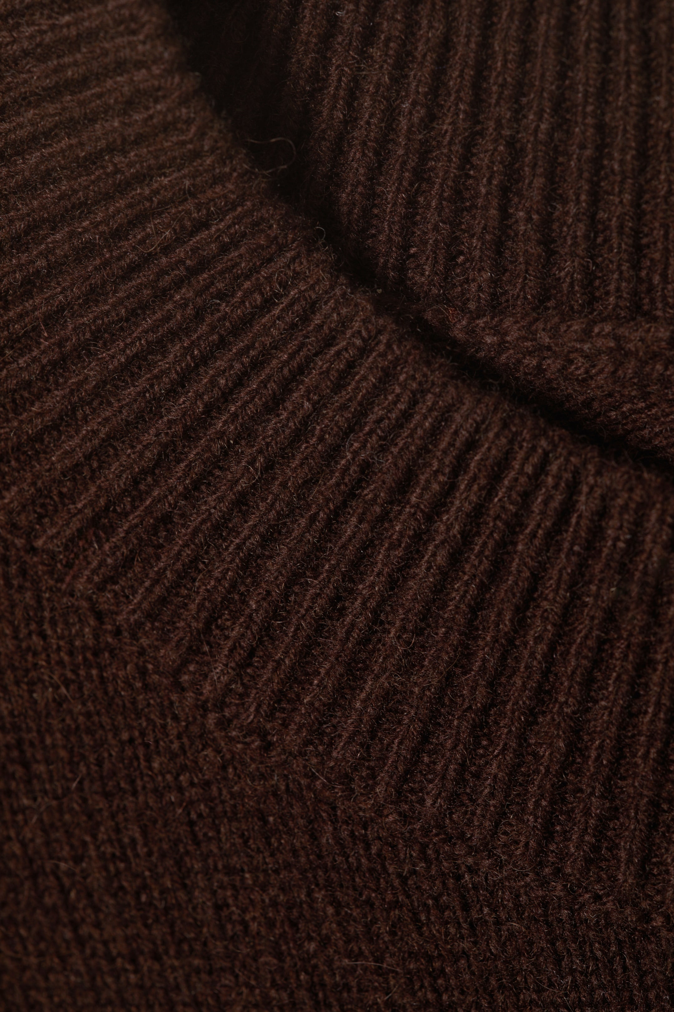 Größeres Bild anzeigen: Ein dunkelbrauner Rippstrickstoff zeigt seine weiche, leicht flauschige Textur und markante vertikale Rippen, mit einer diagonalen Naht sichtbar, wo zwei gerippte Abschnitte zusammengefügt werden.