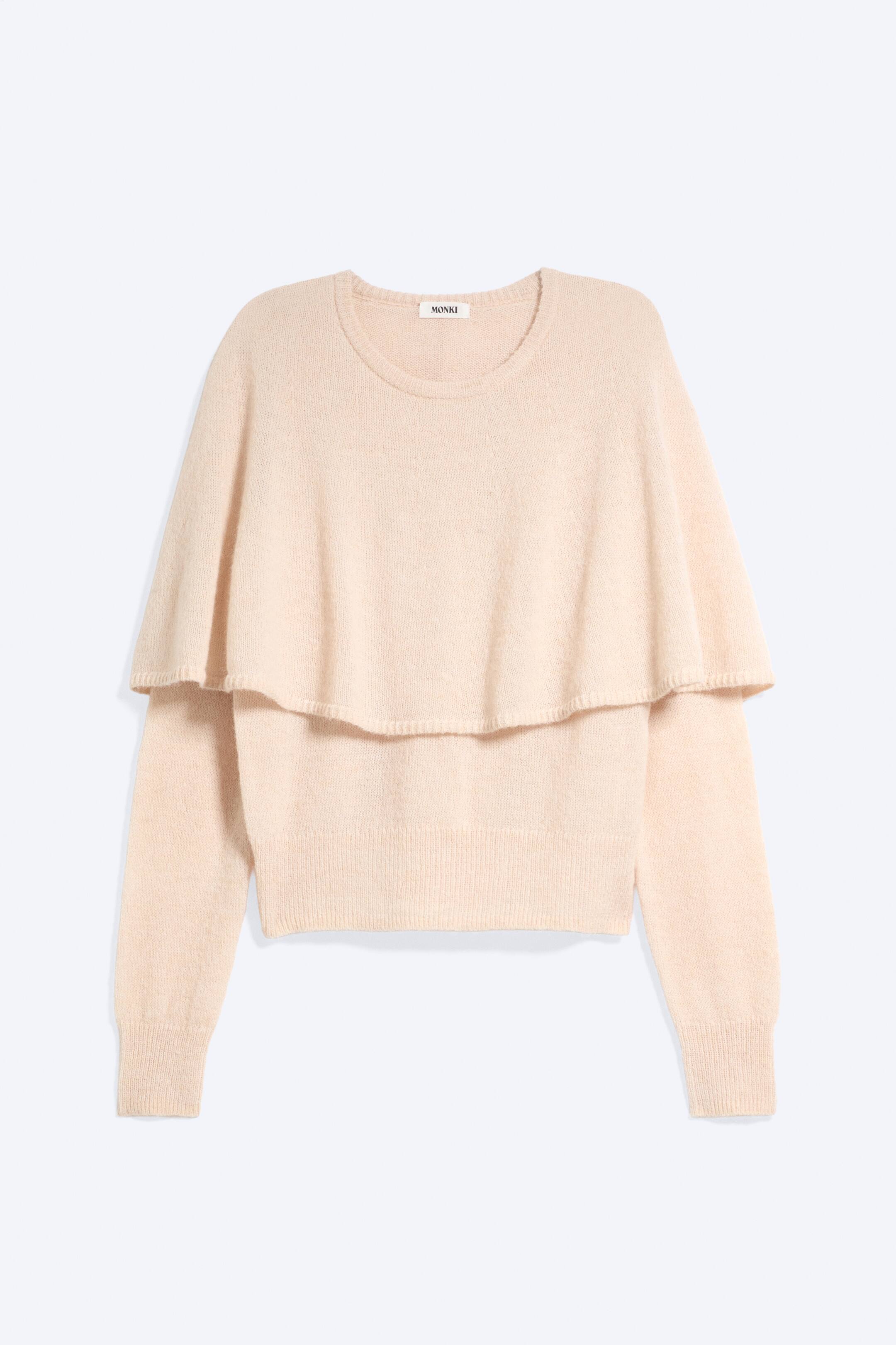 Größeres Bild ansehen: Ein hell pfirsichfarbener Strickpullover ist von vorne zu sehen, mit rundem Ausschnitt, langen Ärmeln mit Rippbündchen und einer integrierten Cape-Überlage, die über die Schultern fällt. Der Pullover ist mit einem Rippbund abgeschlossen.