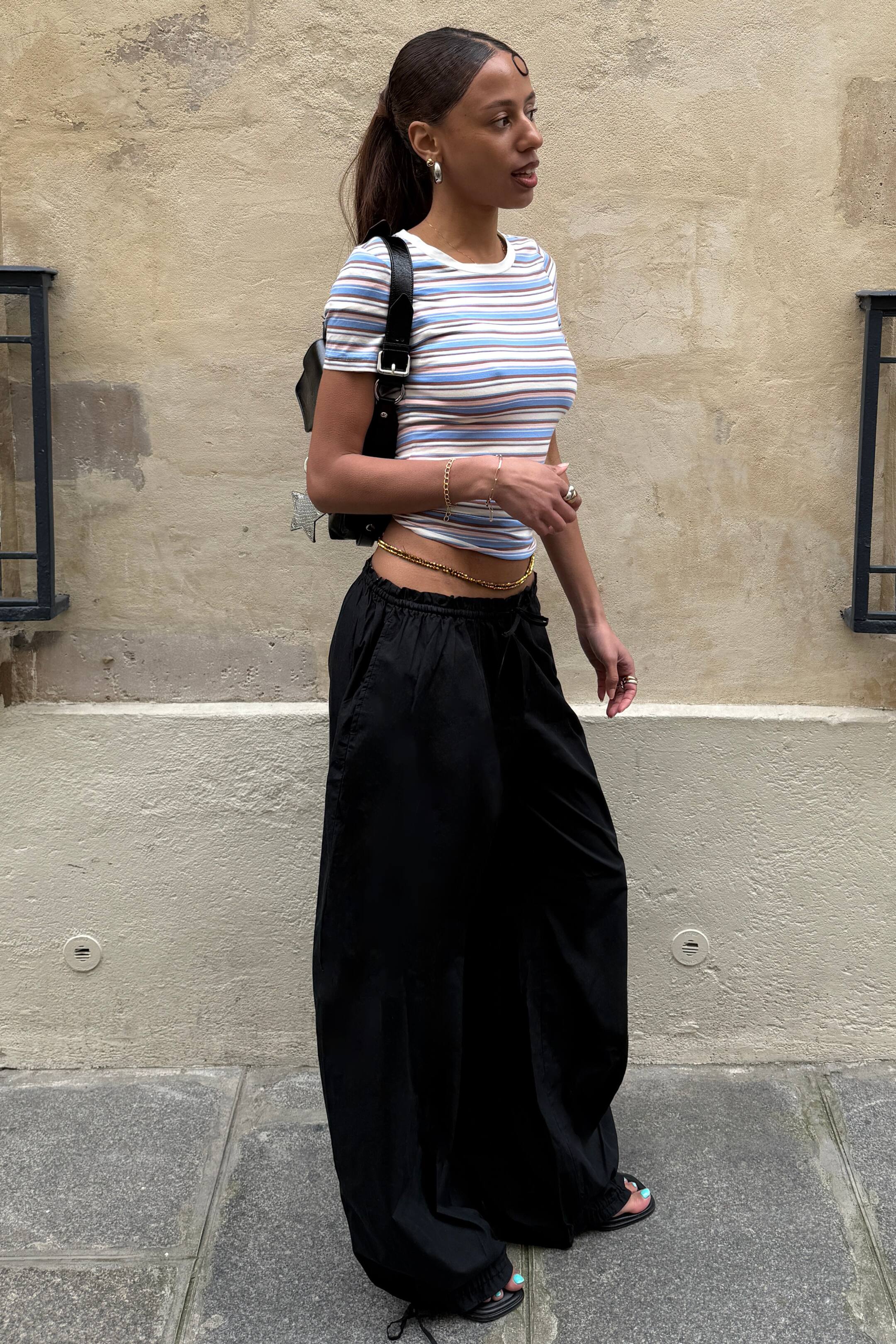 Visa större bild: Svarta vida byxor med elastisk dragsko i midjan och sidofickor, som ger en avslappnad, flödande silhuett från sidan. Byxorna är åtdragna vid anklarna med synliga dragsnören, vilket skapar en rynkad effekt över skorna.