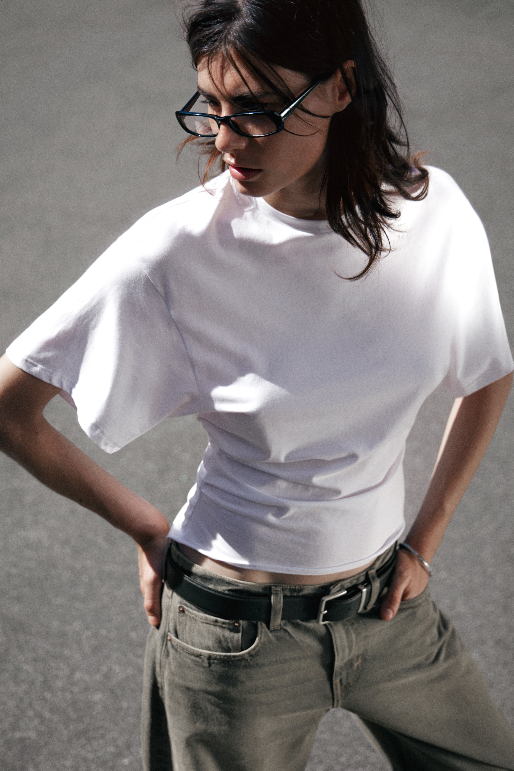 View larger image: A white crew neck t-shirt is being worn, featuring a relaxed, slightly oversized fit through the body and short, wide-cut sleeves, with its hem being tucked into dark pants to create a bloused effect at the waist.