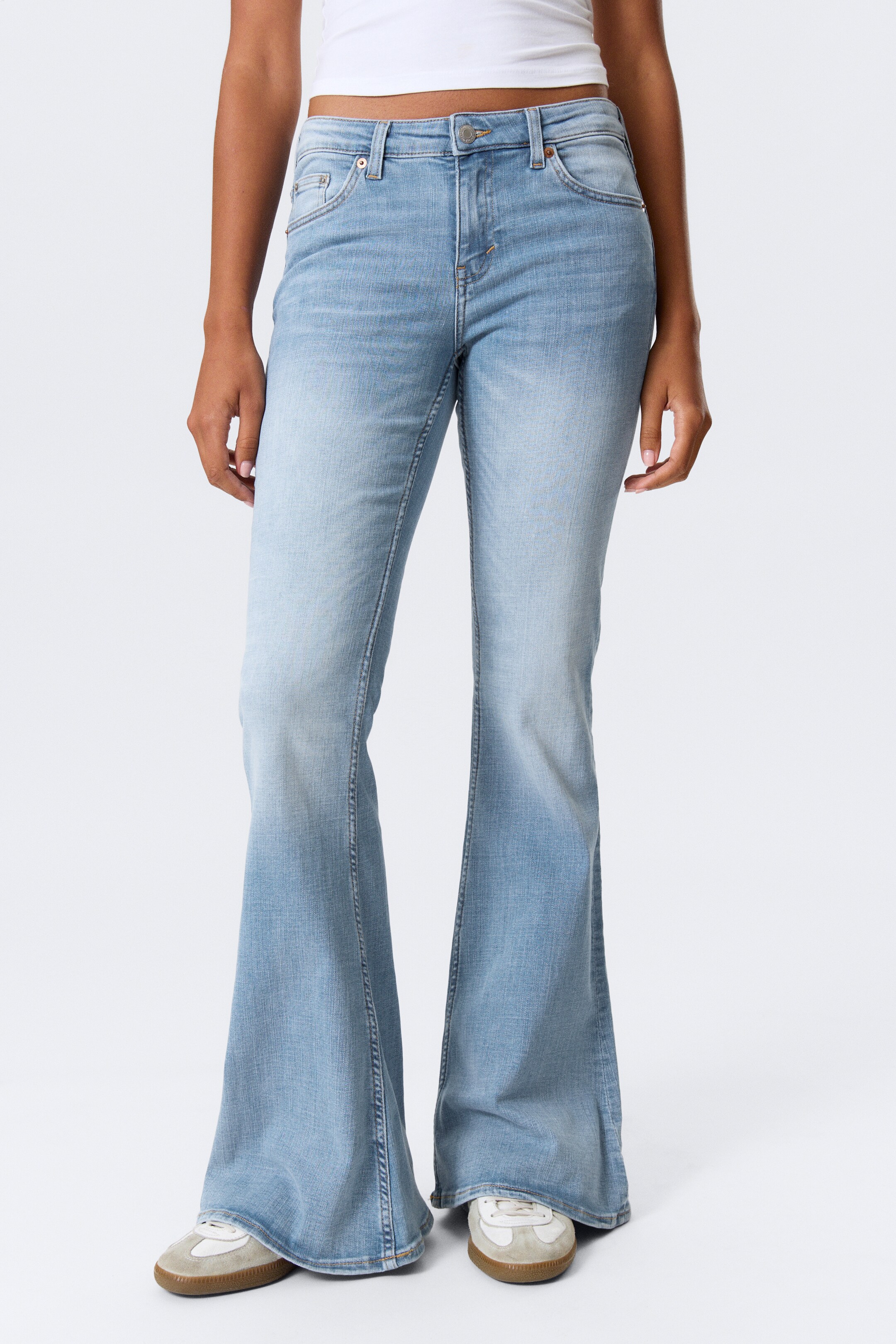 View larger image: Light blue denim flare jeans are being presented from the front, featuring a high-waisted design with classic five-pocket styling, a prominent wide flare extending from the knee, and subtle fading visible on the upper thighs and seat.