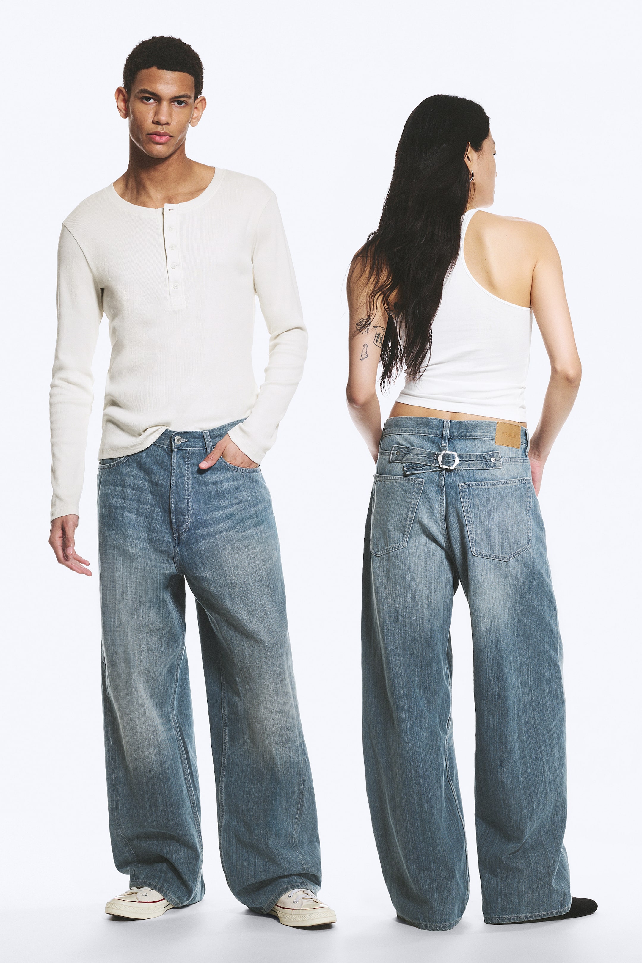 Größeres Bild anzeigen: Ein Paar blaue Denim-Jeans wird sowohl von vorne als auch von hinten gezeigt. Die Vorderansicht zeigt eine weite Passform, eine verwaschene Optik, einen Knopfverschluss und Vordertaschen. Die Rückansicht präsentiert ein Schnallendetail am Bund und aufgesetzte Gesäßtaschen.