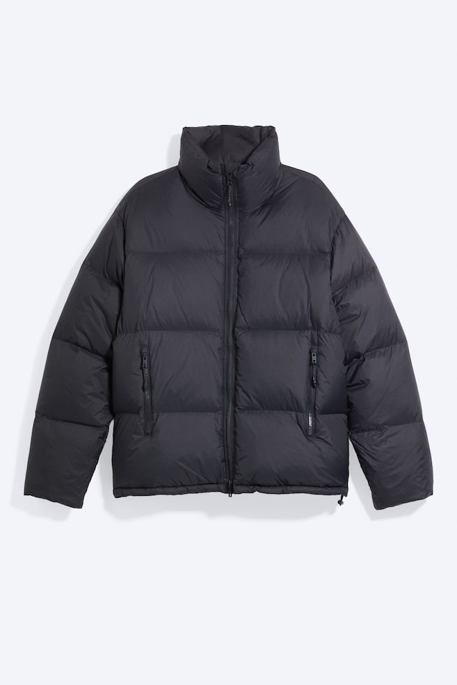 Eine schwarze Pufferjacke in lockerer Passform ist von vorn zu sehen und verfügt über eine horizontale Steppung, einen hohen Stehkragen sowie einen mittigen Zwei-Wege-ReiÃverschluss. Die Jacke zeigt ReiÃverschlusstaschen vorne und einen sauberen Saum mit dezentem Kordelzugdetail. - 1