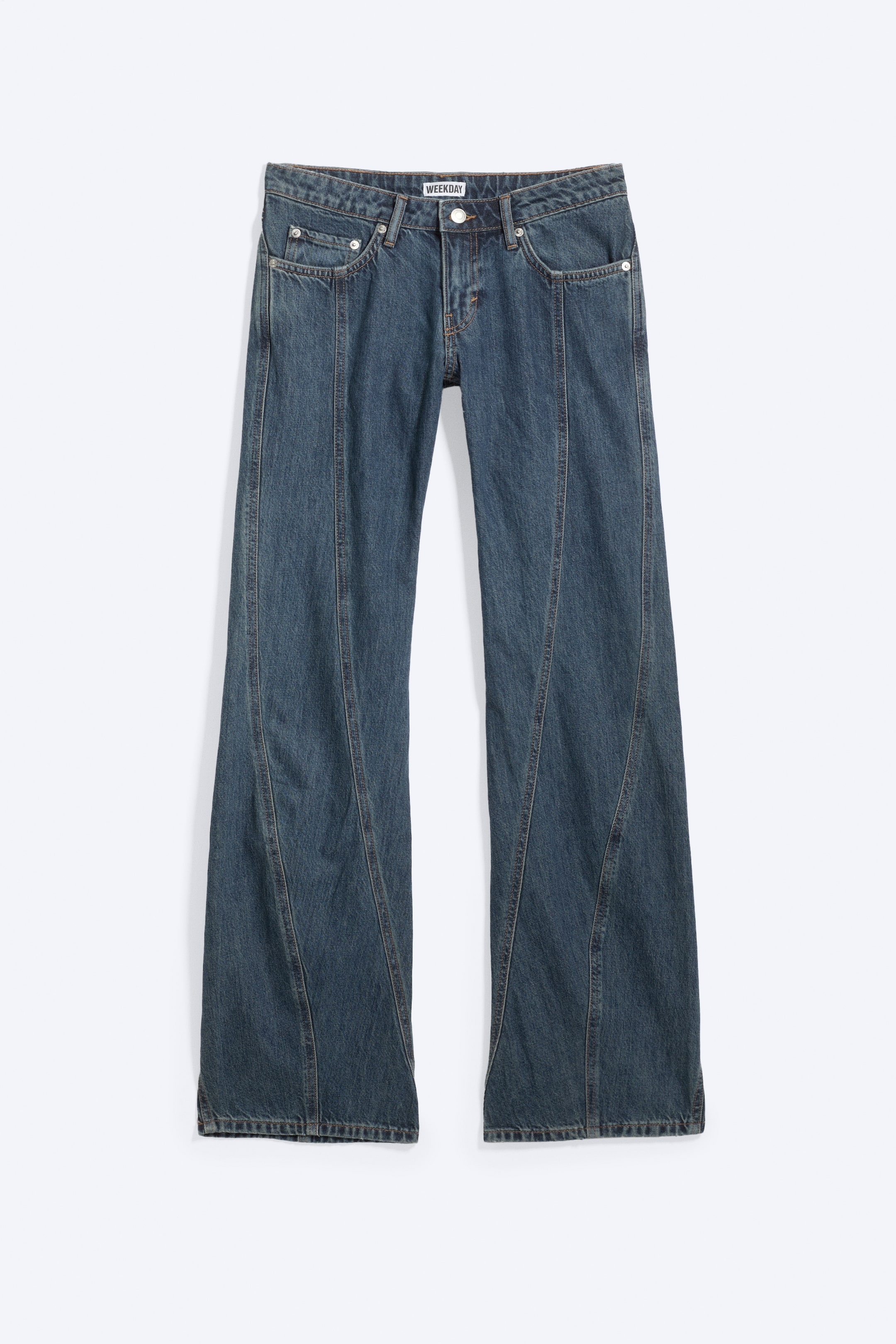 Agrandir l'image: Un jean en denim bleu est présenté de face, avec une coupe large et une taille avec passants pour ceinture, une fermeture à bouton et une braguette zippée. Les poches avant avec rivets sont visibles, et une couture incurvée descend au centre de chaque jambe.
