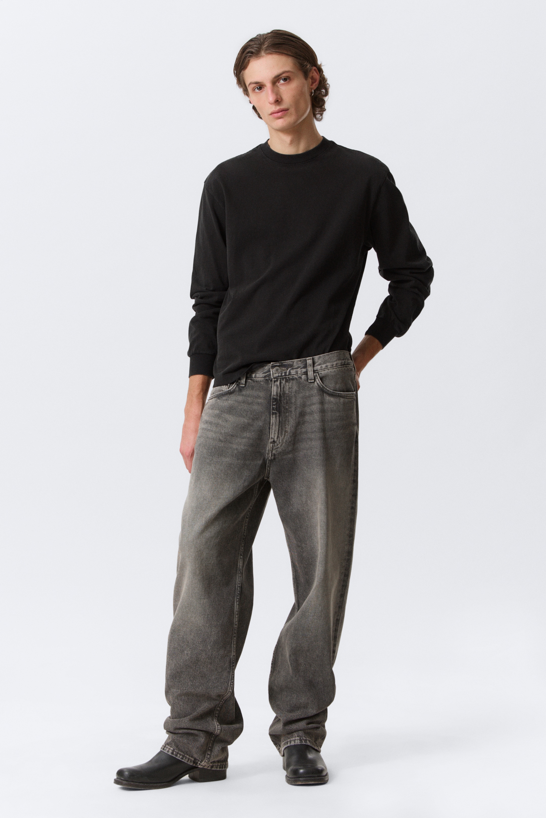 Größeres Bild ansehen: Dunkelgraue, locker sitzende Jeans werden frontal, leicht nach links geneigt präsentiert, mit einem gewaschenen Finish, einer mittelhohen Taille und weiten Beinen, die sich über schwarze Schuhe legen.