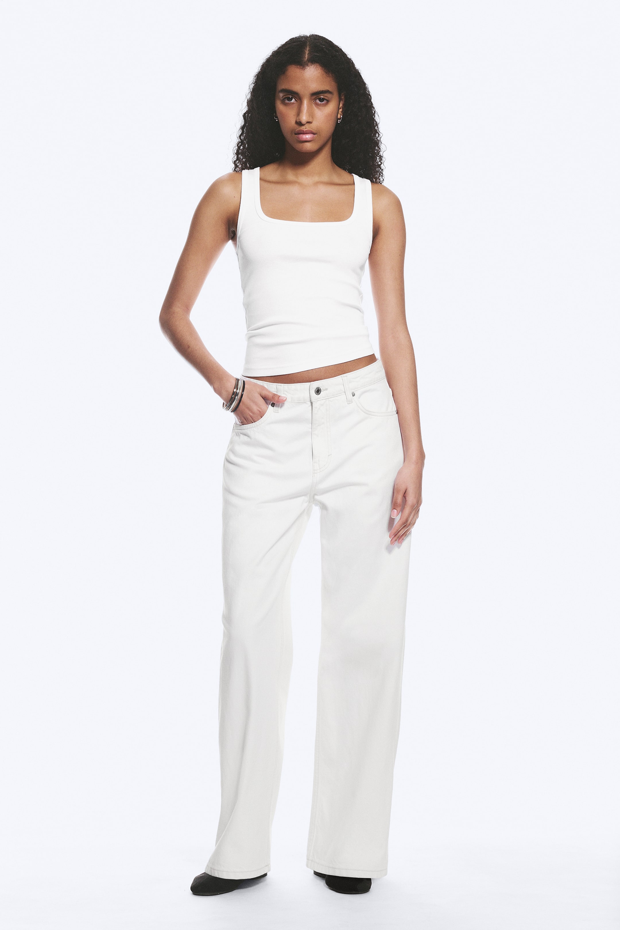 Grotere afbeelding bekijken: Een witte geribbelde tanktop met een vierkante halslijn en een aansluitende pasvorm. Het wordt gedragen met witte jeans met wijde pijpen, die een vijfzakkenstijl en een volledige lengte tonen.
