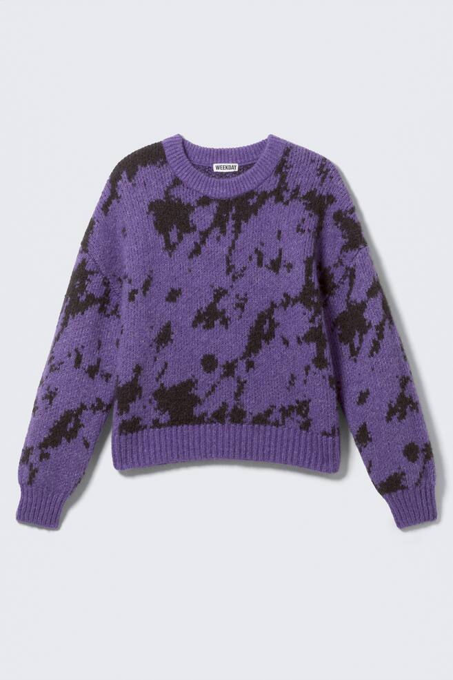 Un maglione, come FRONT, presenta una base viola con un motivo maculato marrone scuro irregolare. È progettato con un girocollo, maniche lunghe, polsini a coste, un orlo a coste e un'etichetta del marchio "WEEKDAY" visibile nella parte posteriore del collo. - 1