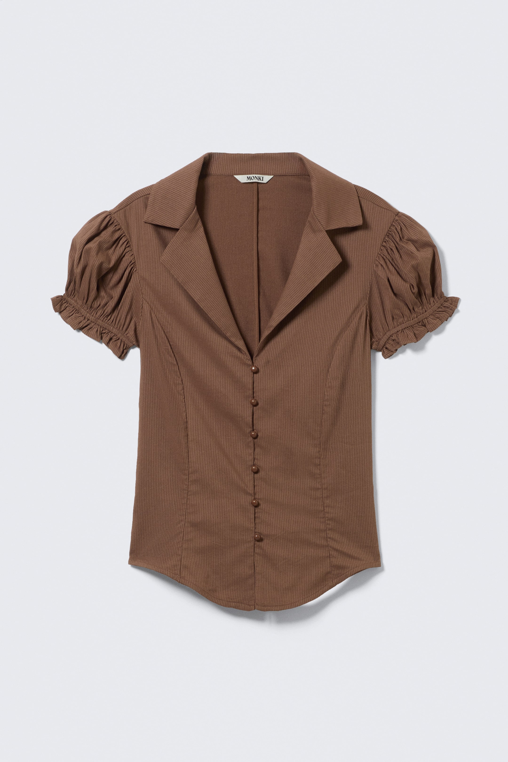 Grotere afbeelding bekijken: Een bruine kortmouwige blouse wordt frontaal gepresenteerd, met een fijne verticale geribbelde textuur, een puntige kraag en een open V-hals. Hij sluit met een volledige knoopsluiting van zeven ronde bruine knopen, en de korte mouwen zijn gepoft bij de schouders en verzameld met elastische ruches bij de manchetten.