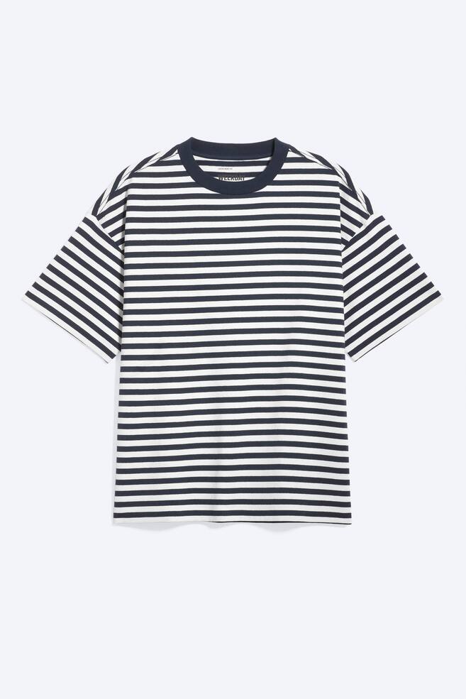 En t-shirt vises forfra med vandrette marineblå og hvide striber. Den er designet med rund hals, nedfaldne skuldre og brede ærmer, hvilket giver en oversized, løs pasform. - 1