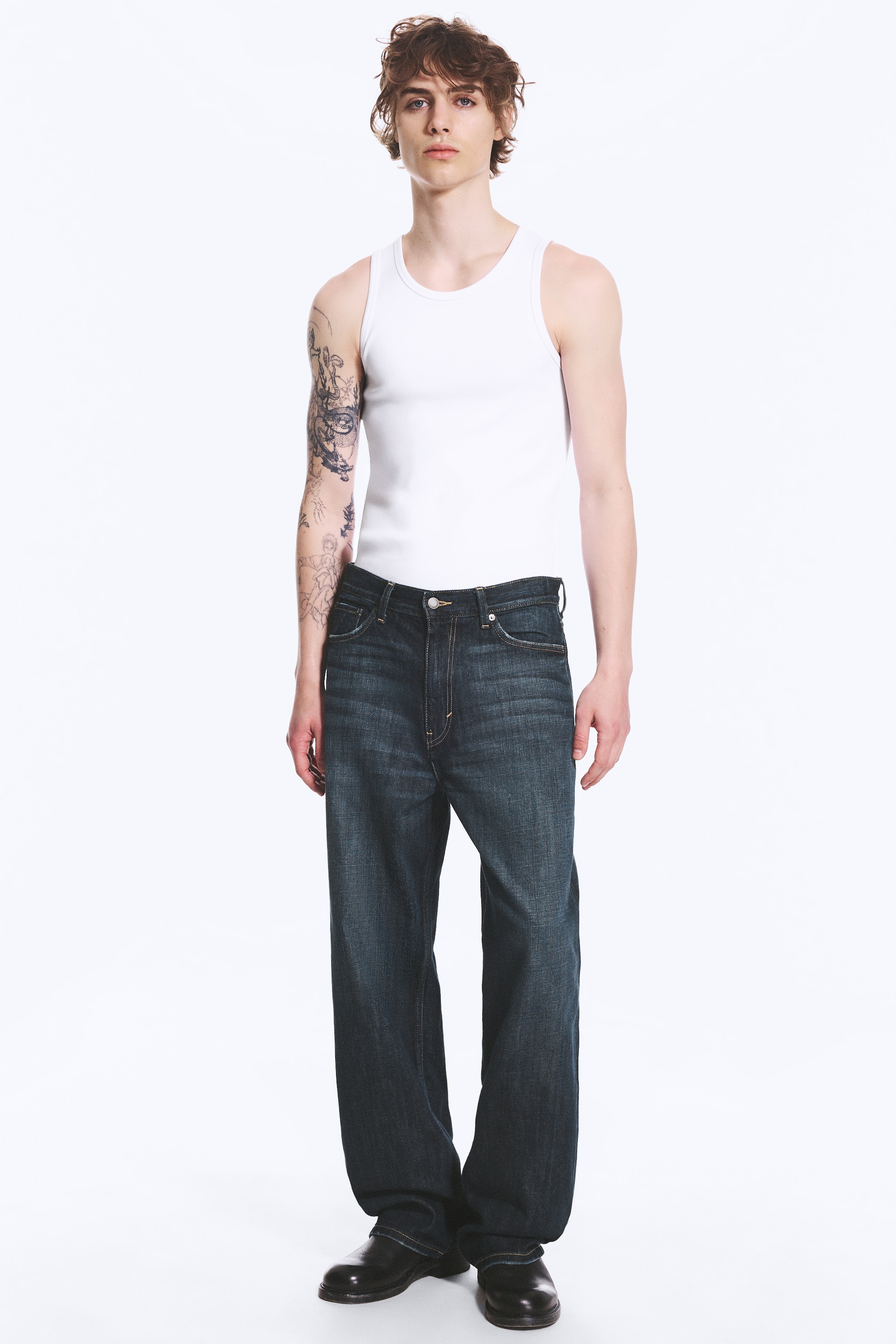 Et par mid-rise, løstsiddende, straight-leg jeans vises i front. De har en mørk vask med diskret falming, et klassisk femlomme-design med en synlig møntlomme og en lynlås med en metal knaplukning.