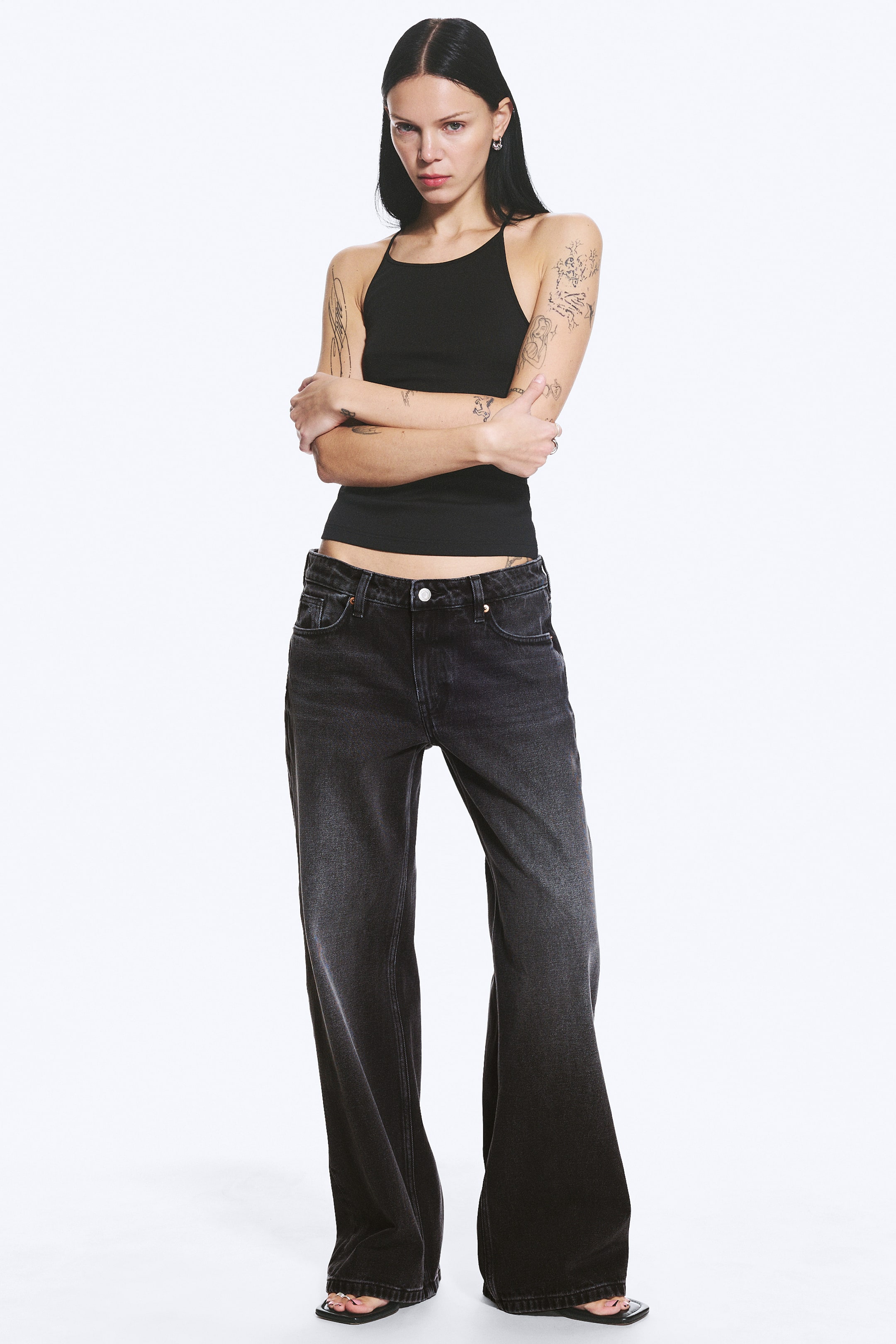 Vis større bilde: Vasket sorte jeans med vide ben har høy midje med knappelukking og et femlommers design, sett fra en frontvinkel. De viser en avslappet passform gjennom benet, som flyter ut i en bred kant.