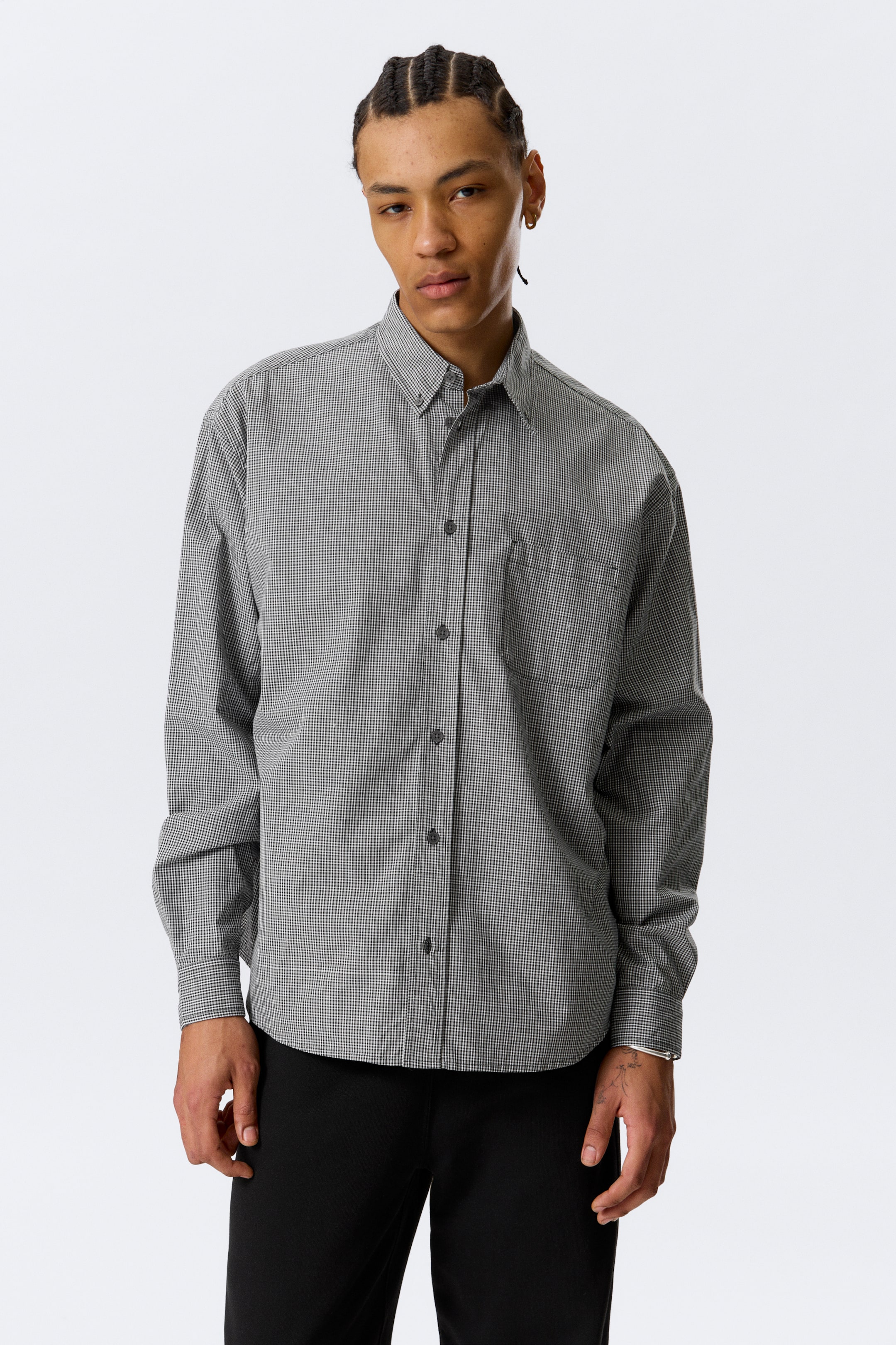 Se større billede: Modellen bærer en løstsiddende, langærmet skjorte med et sort og hvidt småternet mønster. Den har en knap-ned krave, knaplukning, faldne skuldre, en brystlomme, knappede manchetter og en buet søm.