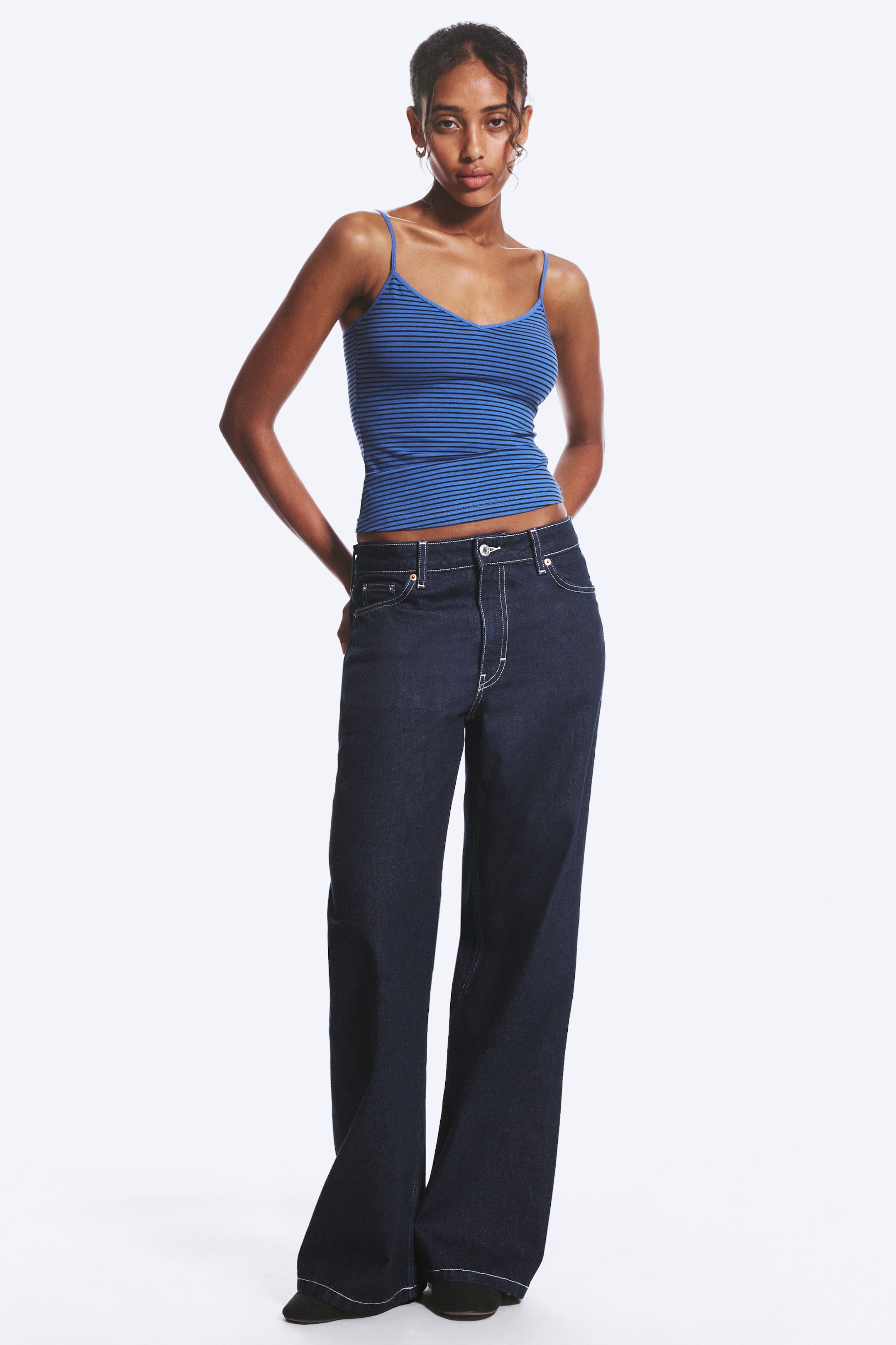 Agrandir l'image: Un jean à jambes larges, taille mi-haute, en denim foncé avec des surpiqûres blanches contrastantes, un design à cinq poches et une fermeture éclair est porté par le mannequin.