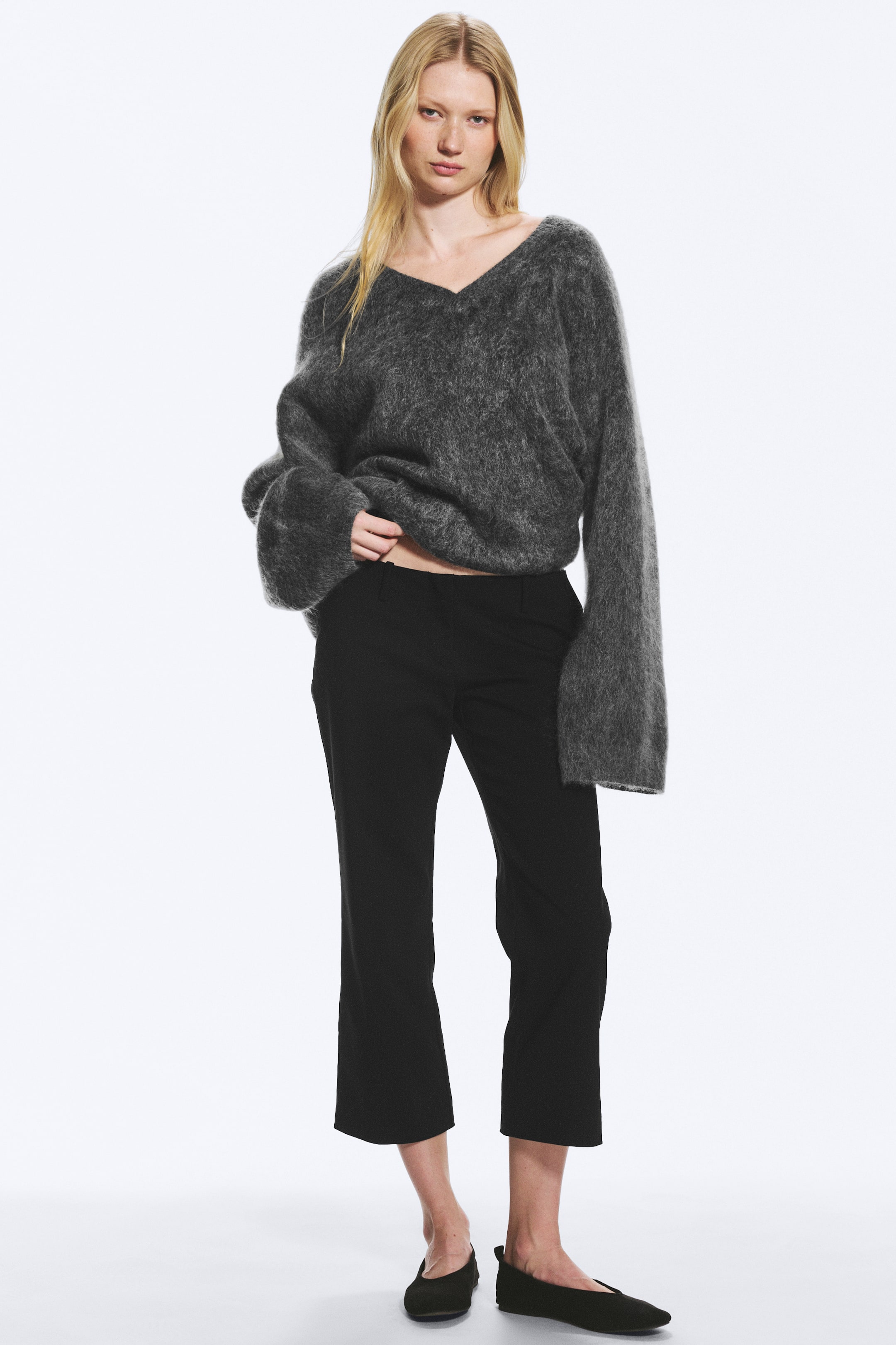 Visualizza l'immagine ingrandita: La modella indossa pantaloni sartoriali neri a vita bassa, dalla vestibilità regolare, con gamba alla caviglia e una leggera silhouette bootcut che si apre verso l’orlo, oltre a tasche laterali oblique ben visibili.