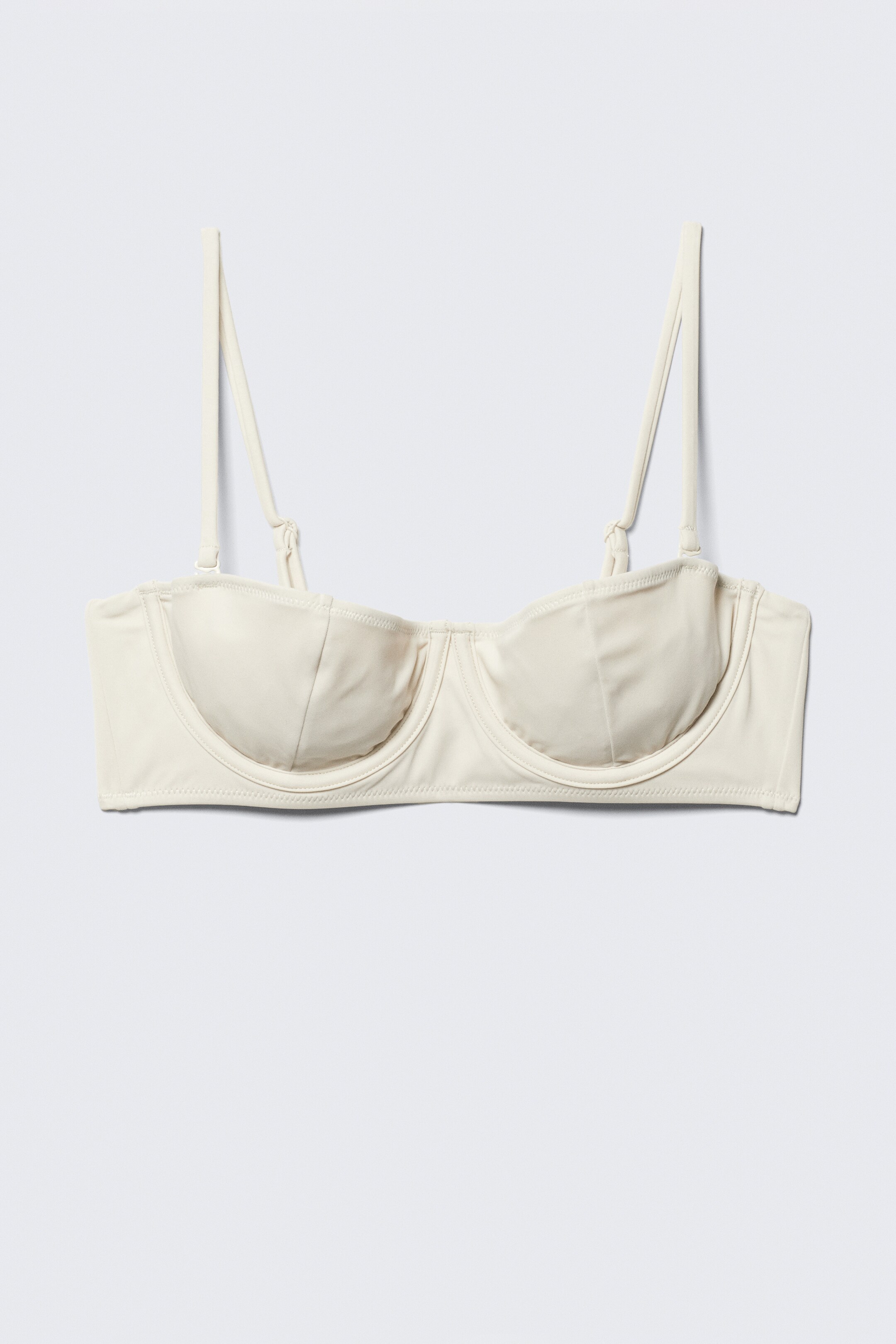 Größeres Bild anzeigen: Ein cremefarbenes Bikini-Oberteil zeigt seine VORDERSEITE. Es verfügt über Bügel-Cups mit einem zentralen Steg und einem glatten Band, das sich zu den Seiten erstreckt. Dünne, verstellbare Träger sind angebracht, mit kleinen sichtbaren Metallverstellern.