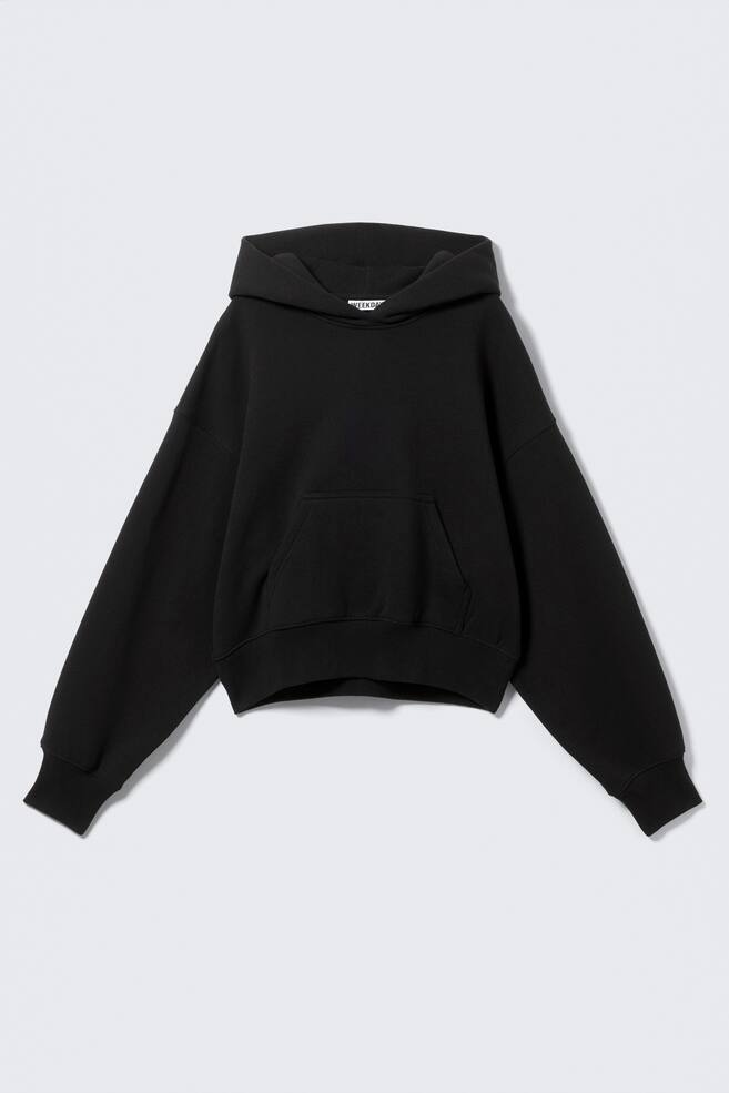 A black hoodie is shown from the FRONT, featuring a boxy, relaxed silhouette with dropped shoulders. It is displaying a roomy hood, a kangaroo pocket, and ribbed trims are visible at the cuffs and hem. - 1