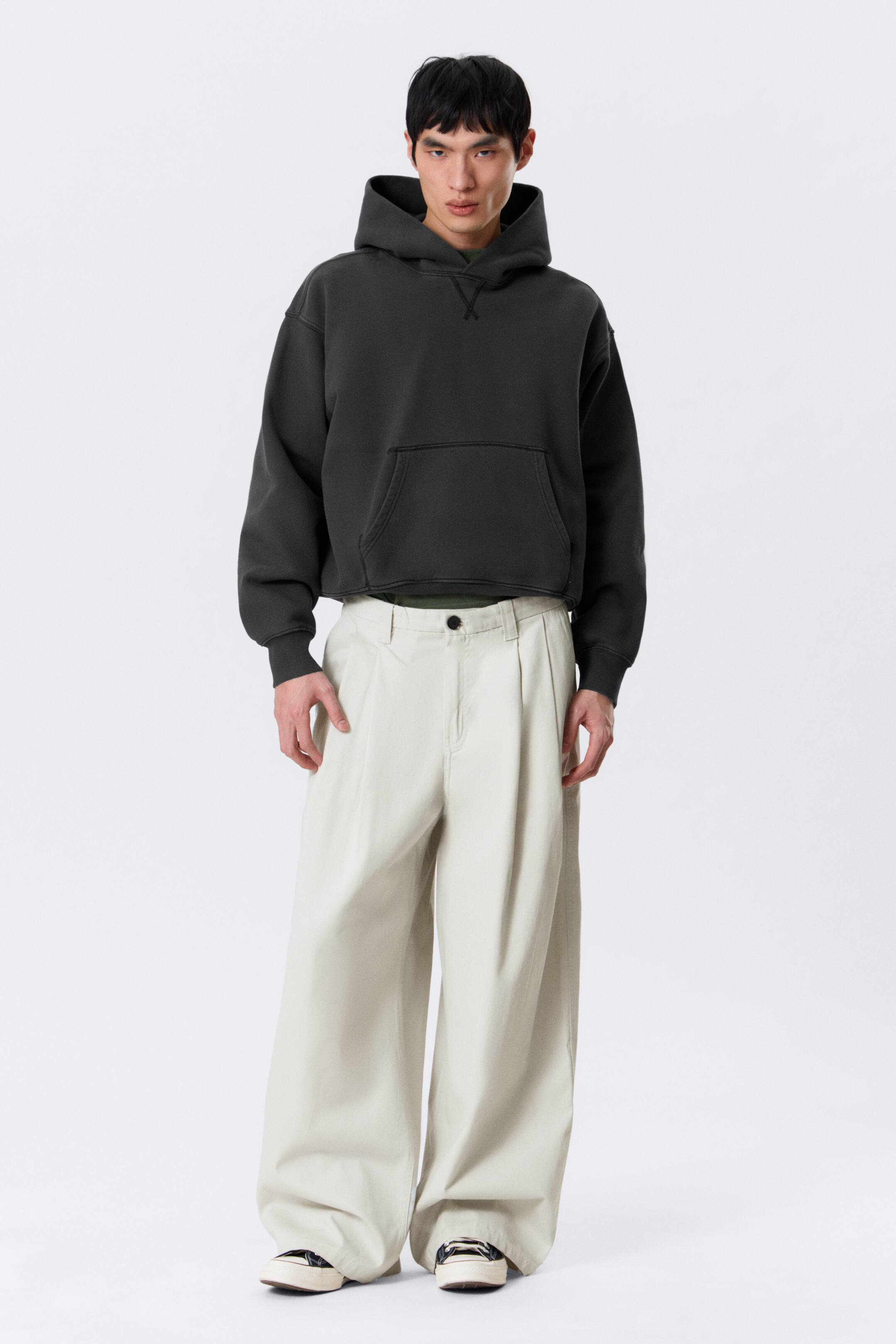 View larger image: A washed dark grey pullover hoodie is being presented, featuring an oversized fit, a structured hood, a front kangaroo pocket, ribbed cuffs, and a ribbed hem. A V-stitch detail is visible below the neckline.