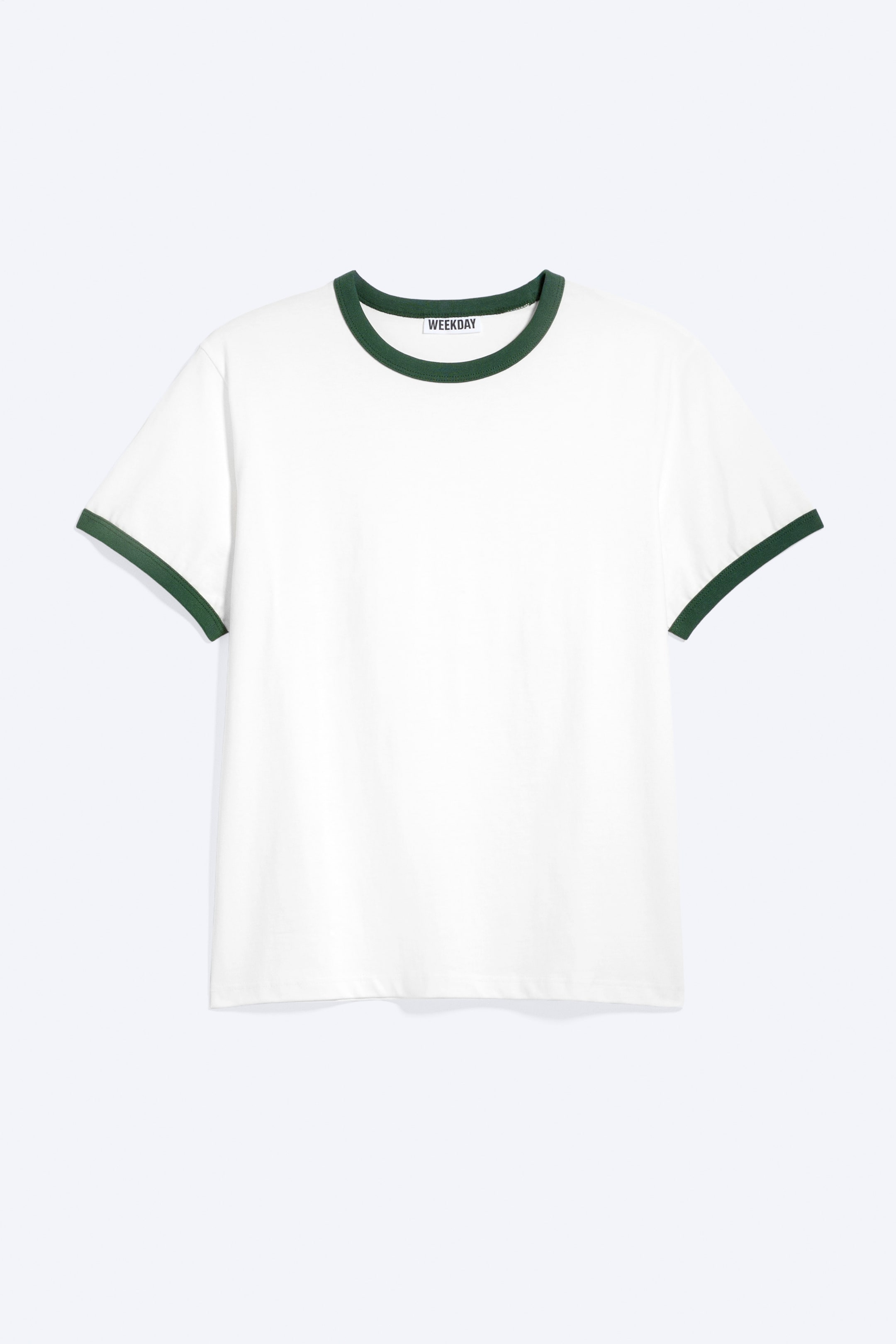 Visa större bild: En vit kortärmad ringer-t-shirt visas framifrån, med mörkgröna kontrastdetaljer på den ribbade kragen och ärmsluten. Ett 'WEEKDAY' varumärkesetikett syns på den inre halslinningen.
