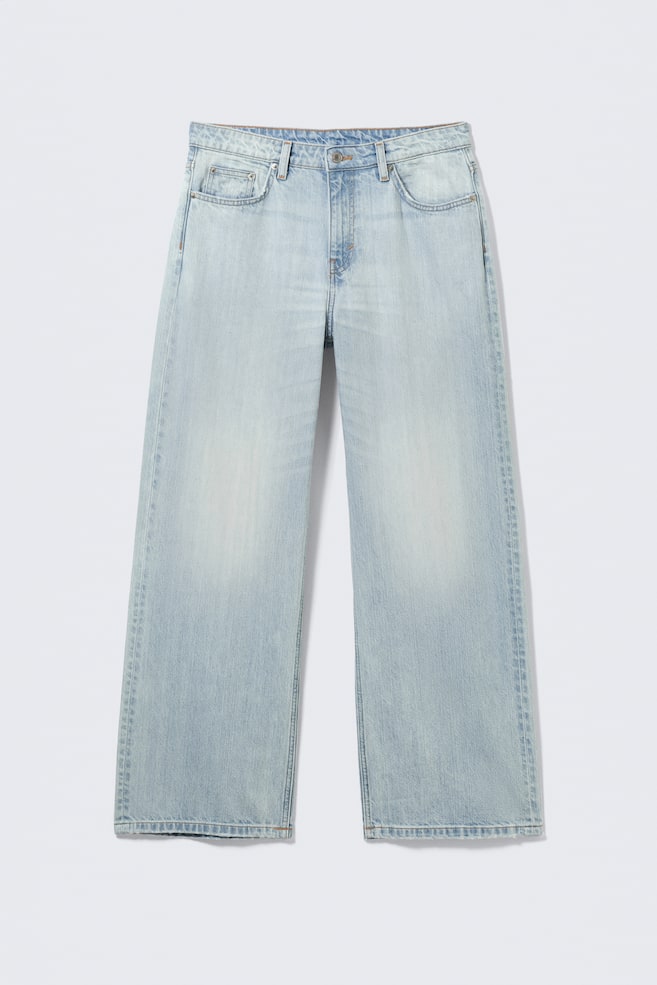 Un jean bleu clair délavé à taille basse est présenté de face, affichant une coupe ample et une jambe droite. Ils sont fabriqués en denim rigide et présentent un design classique à cinq poches, une fermeture éclair et des jambes spacieuses. - 1