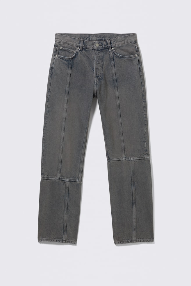 Grey denim jeans are presented facing forward, featuring a button fly, front pockets, and vertical seams running down the front of each leg, with horizontal seams visible across the knees creating a paneled design. - 1