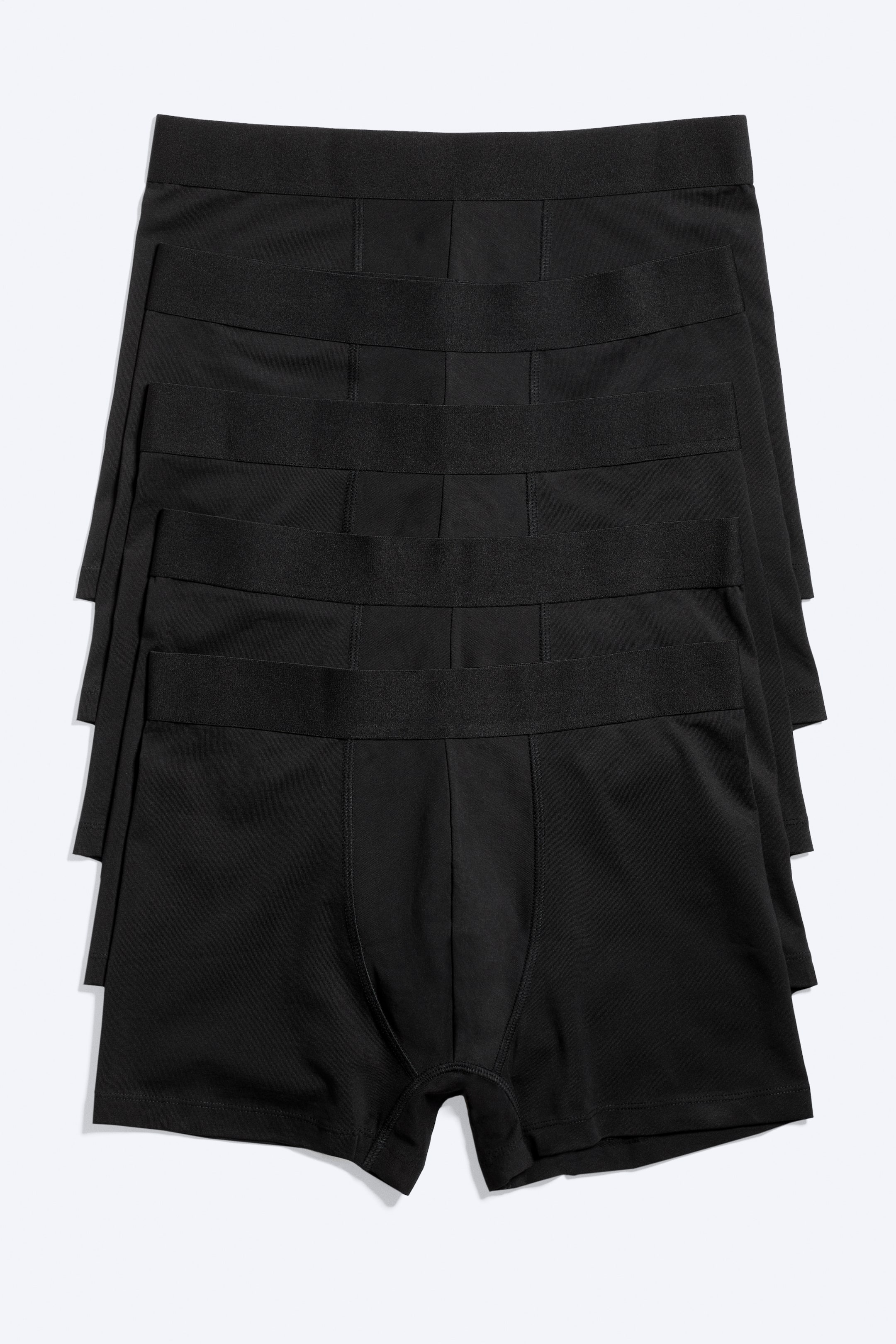 Agrandir l'image: Les boxers noirs sont empilés par lot de quatre, avec la paire du dessus orientée vers l'avant. Ils présentent une ceinture élastique noire lisse et une poche avant profilée, soulignée par des coutures ton sur ton.